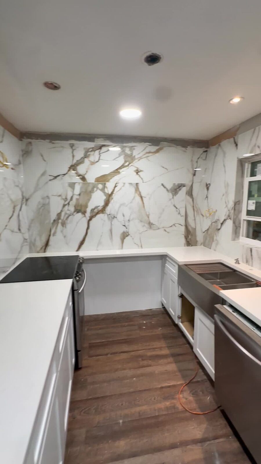 After: Completed floor-to-ceiling Calacatta porcelain kitchen installation with white cabinets and marble-look tile covering all three kitchen walls