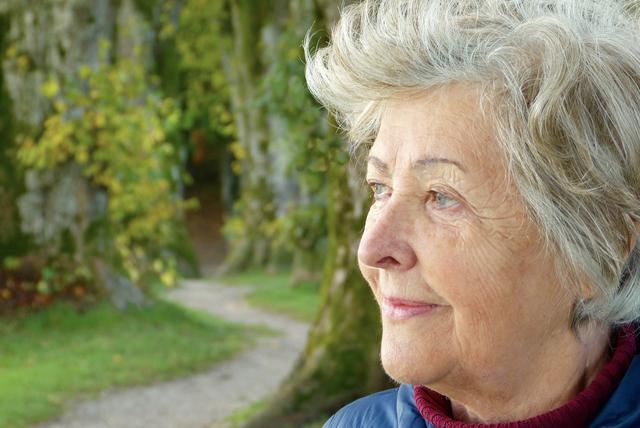 Elderly woman with white hair looking out a garden
