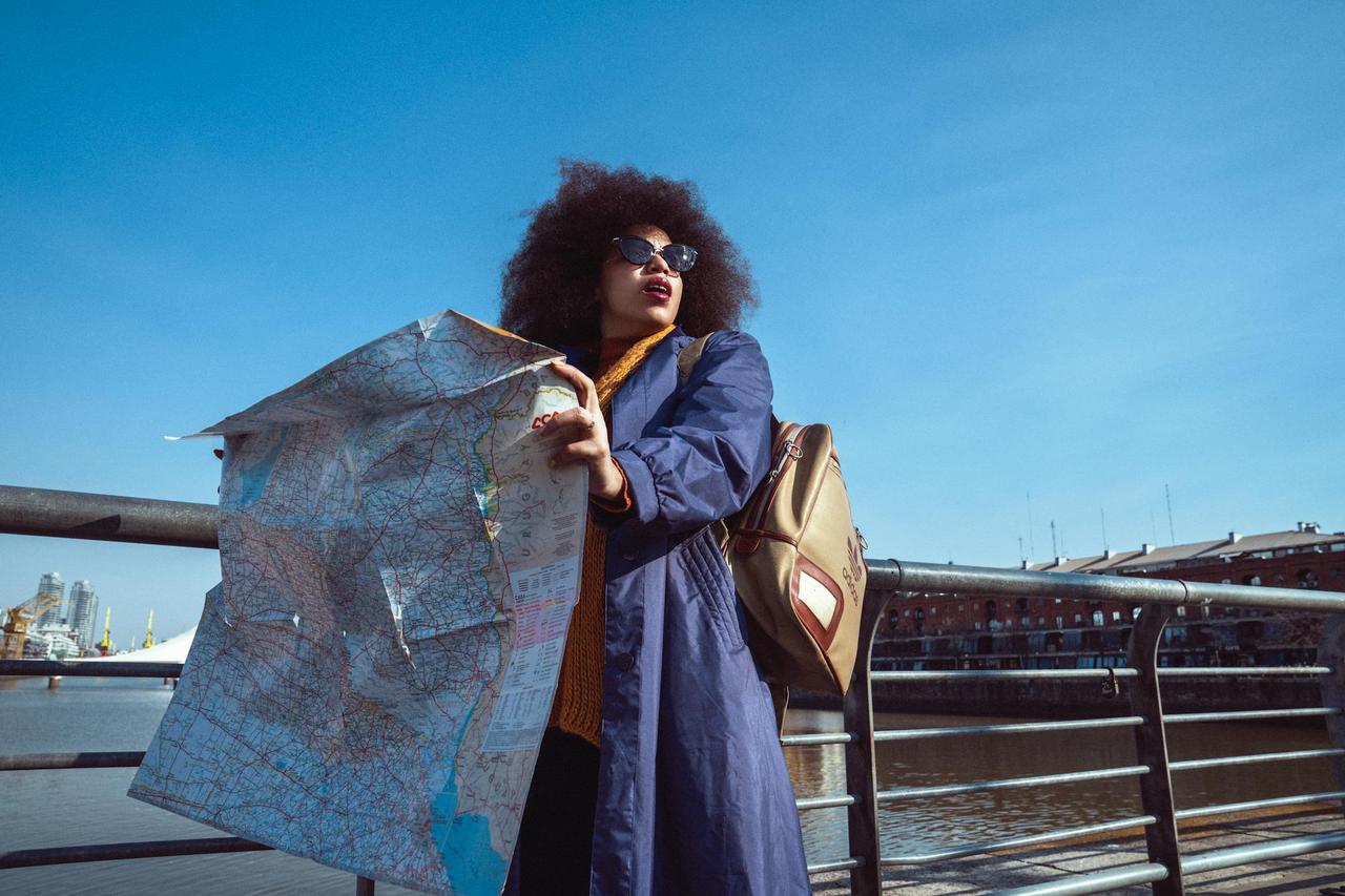 African American woman holds a map on a sunny day by the river, showcasing her adventurous spirit.