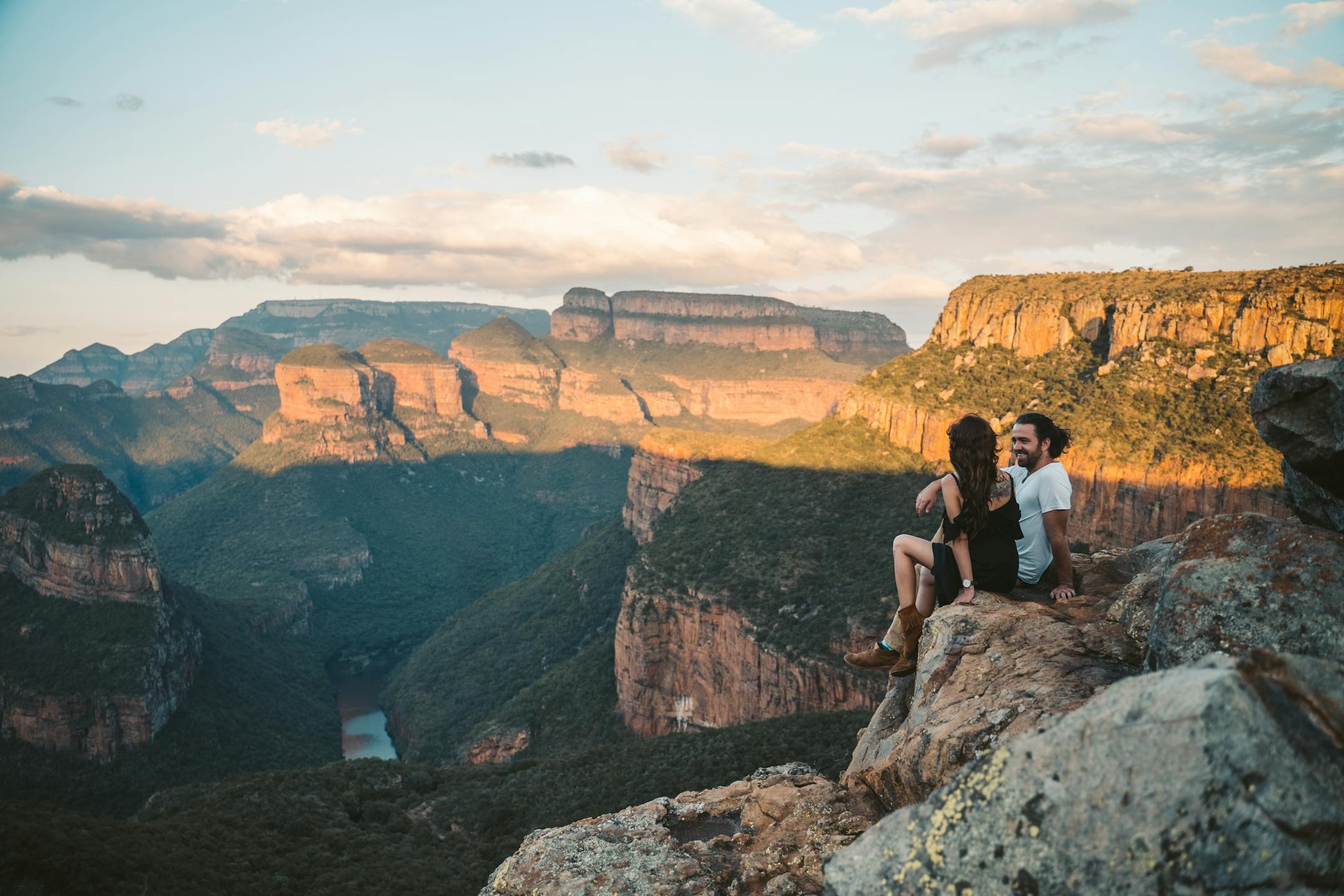 A couple sits on a rocky cliff, enjoying a breathtaking canyon view during sunset, capturing romance and adventure.
