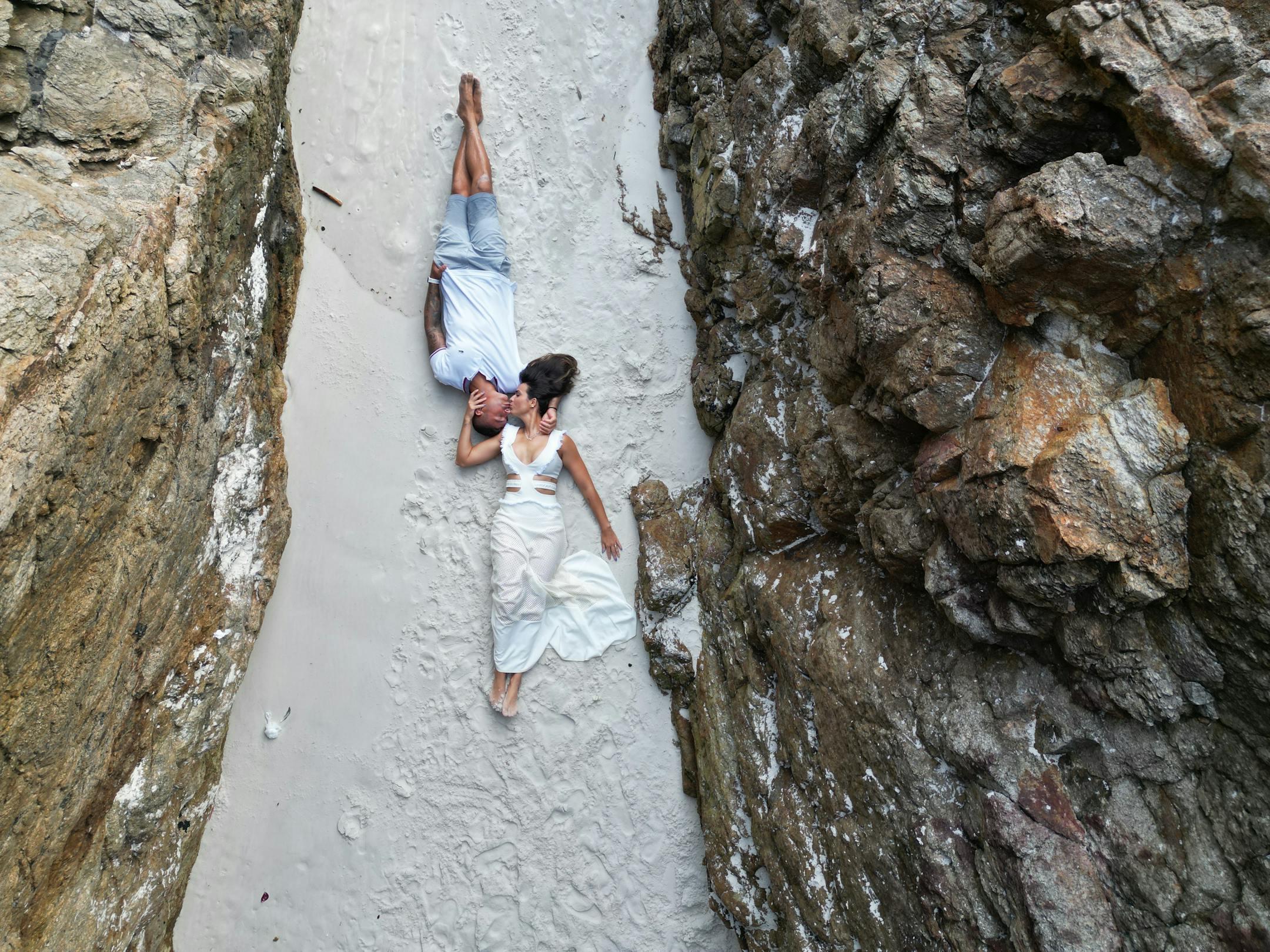A couple embraces on a sandy beach between rocky cliffs, showcasing love and togetherness.