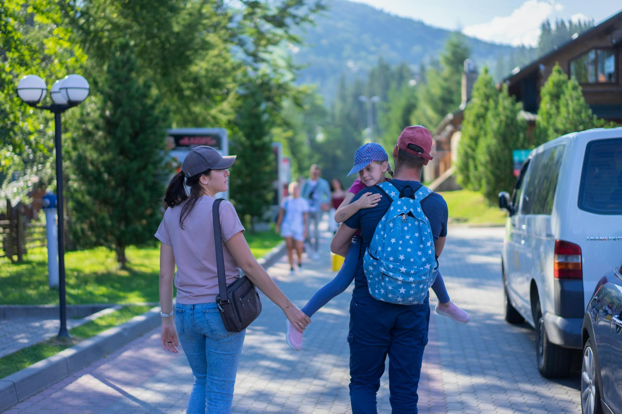 Parents walking with their daughter in a picturesque mountain village, enjoying a sunny day outdoors.