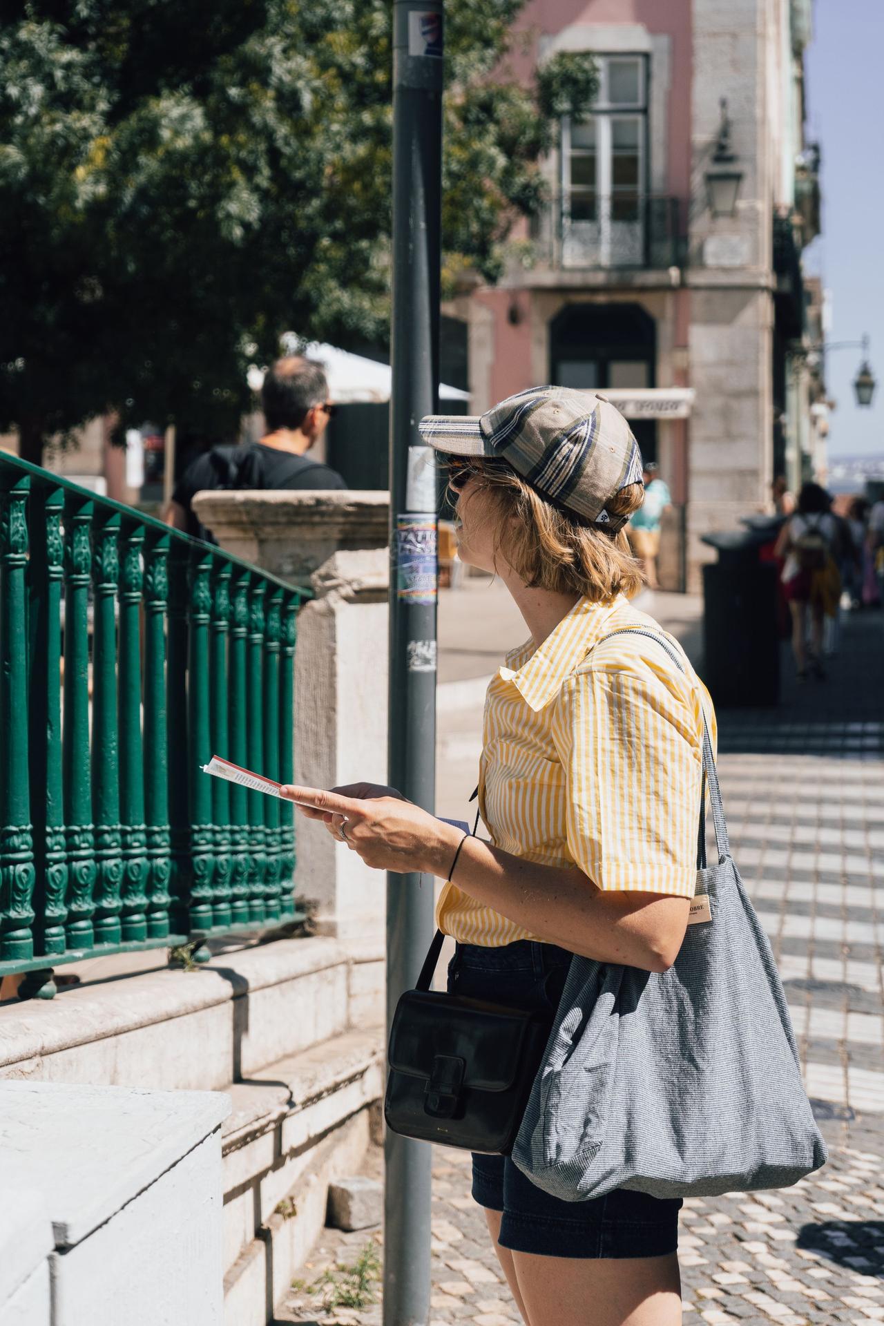 Woman sightseeing in Lisbon, Portugal, holding a guide leaflet on a sunny day.