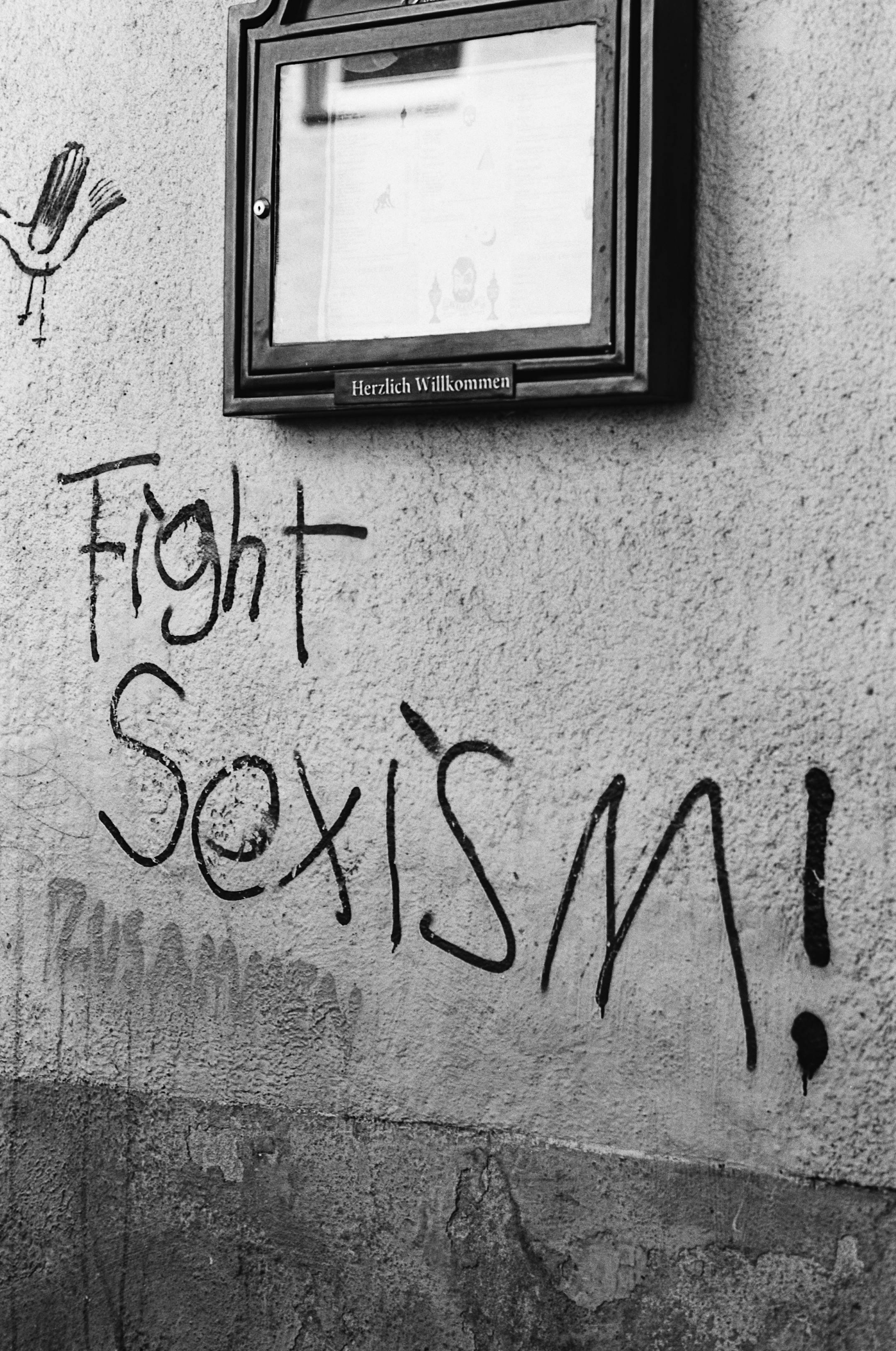 Black-and-white photo of graffiti urging to fight sexism on a street wall.