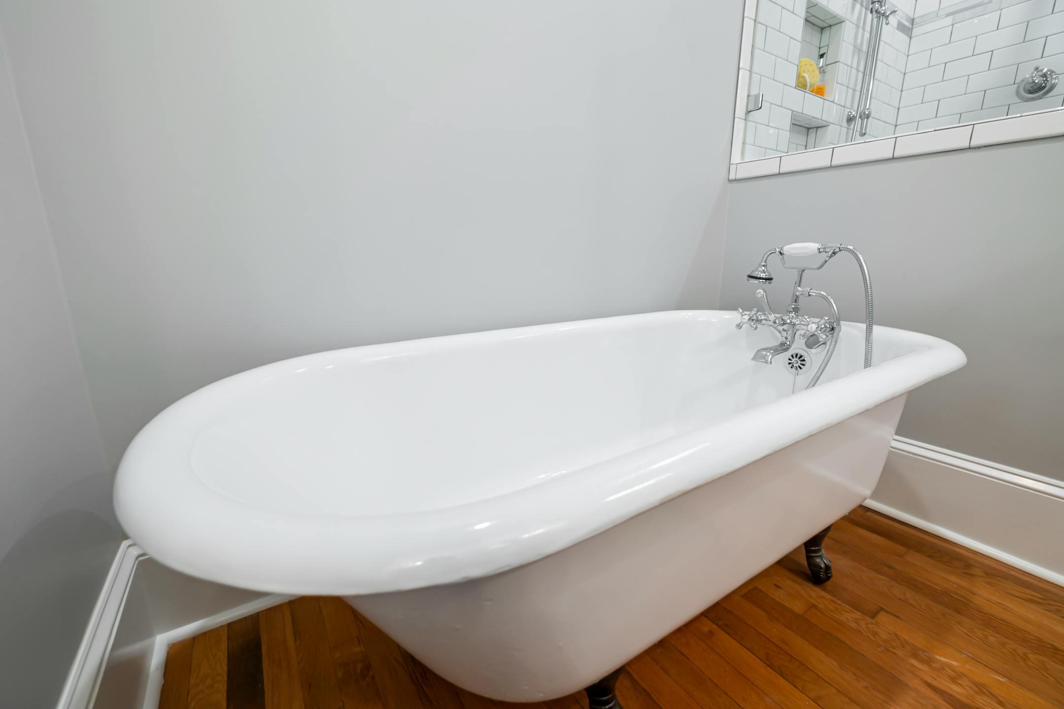 Stylish vintage bathtub with chrome faucet and wooden floor in a modern bathroom.
