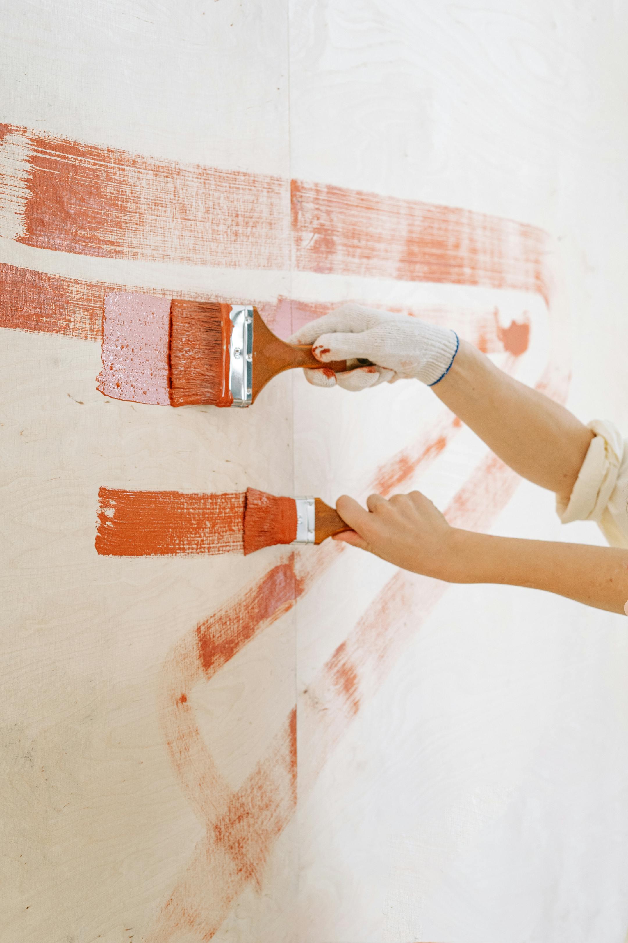 Close-up of hands painting a wall with red strokes, emphasizing DIY home renovation.