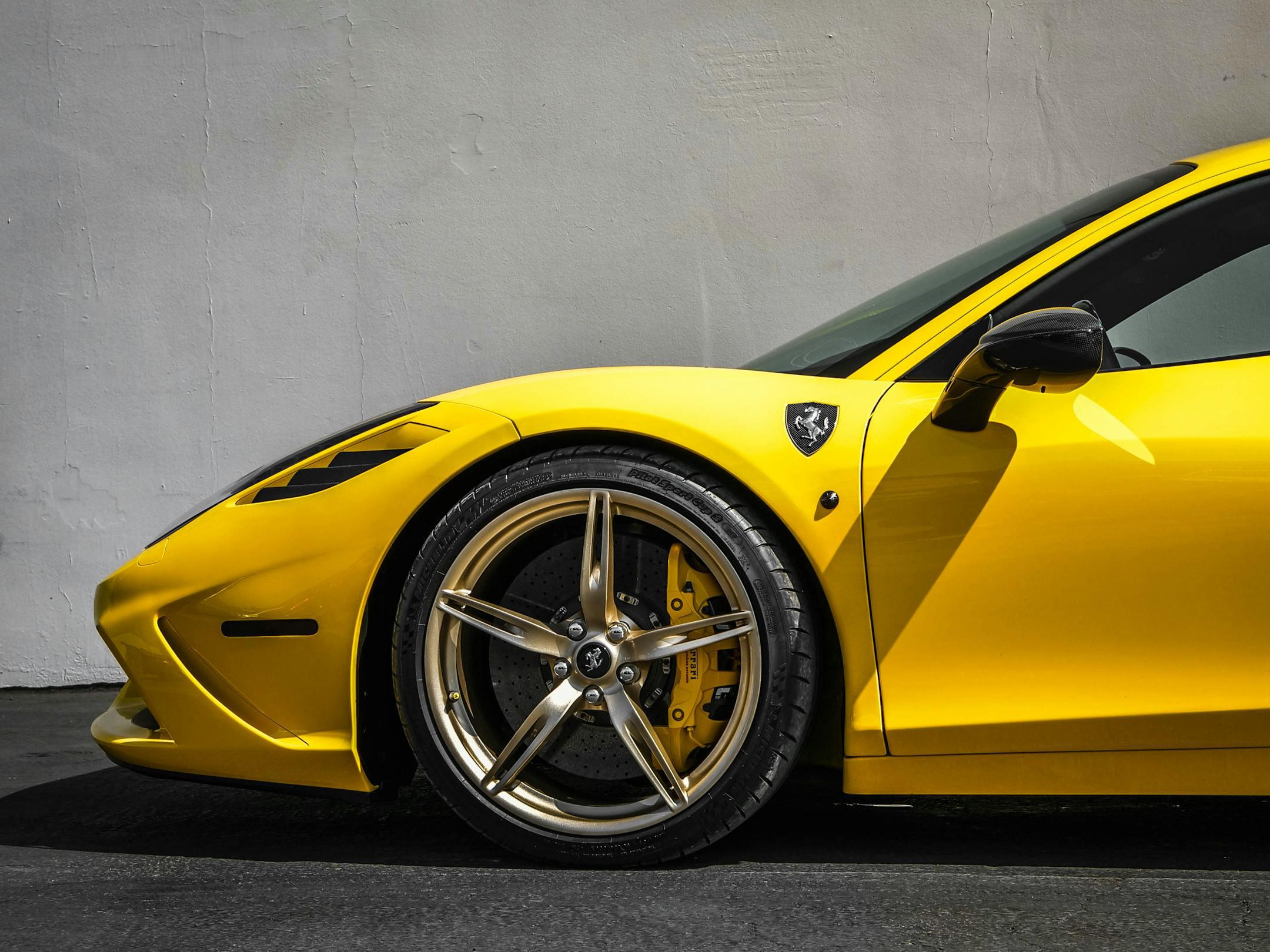 Close-up of a yellow sports car's front wheel and body design against a modern backdrop, exuding luxury.