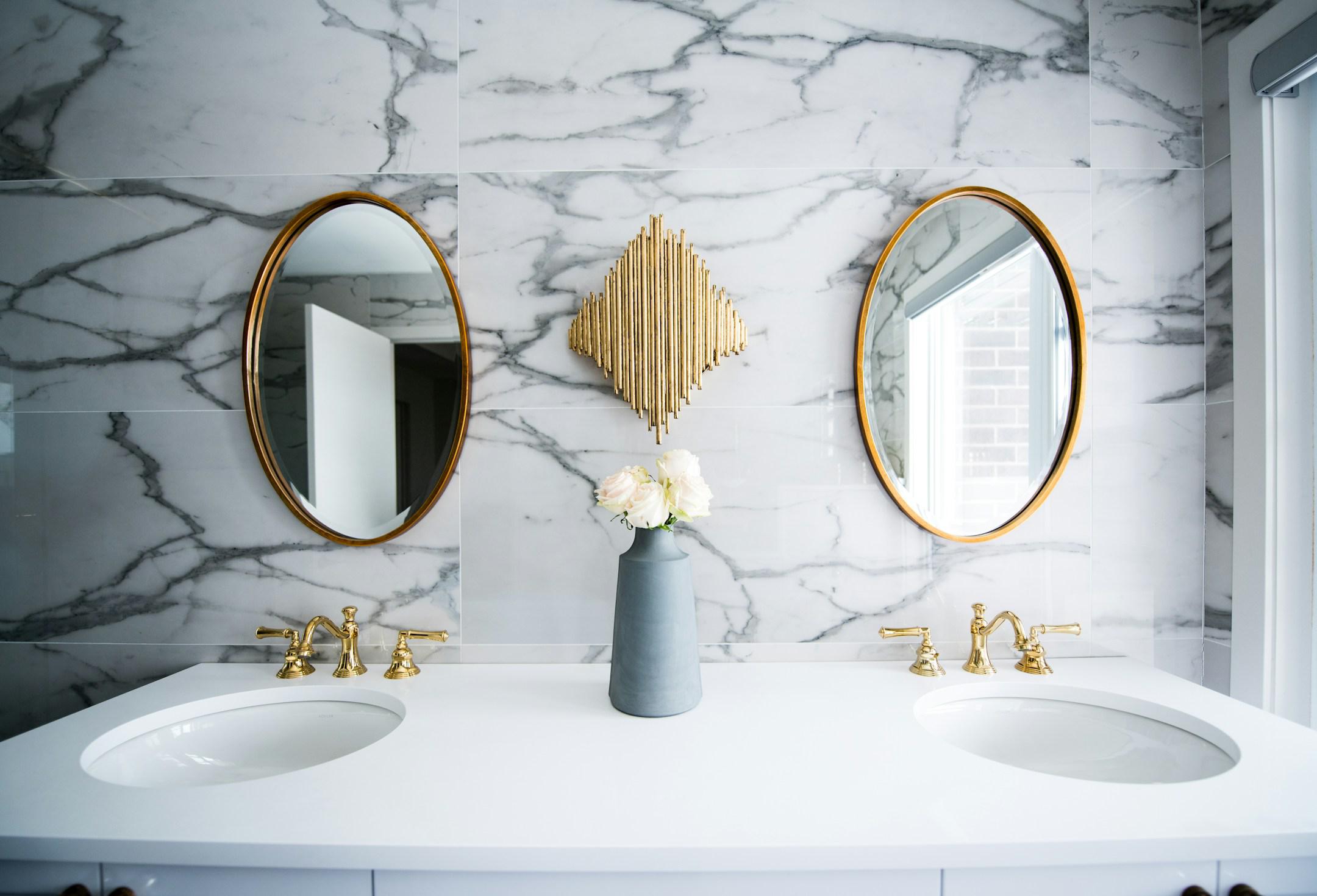 Bright marble and gold bathroom with two sinks and two mirrors.