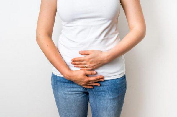 A woman in a white shirt and jens holding her stomach.