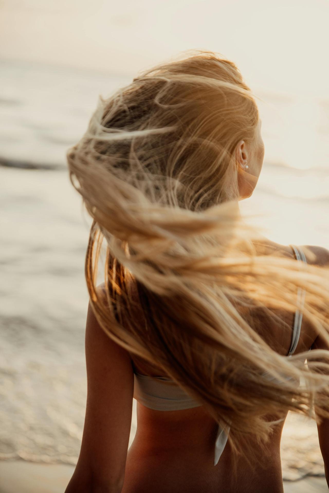 A young woman enjoying a breezy day on a Bali beach with her hair flowing in the sunlight.
