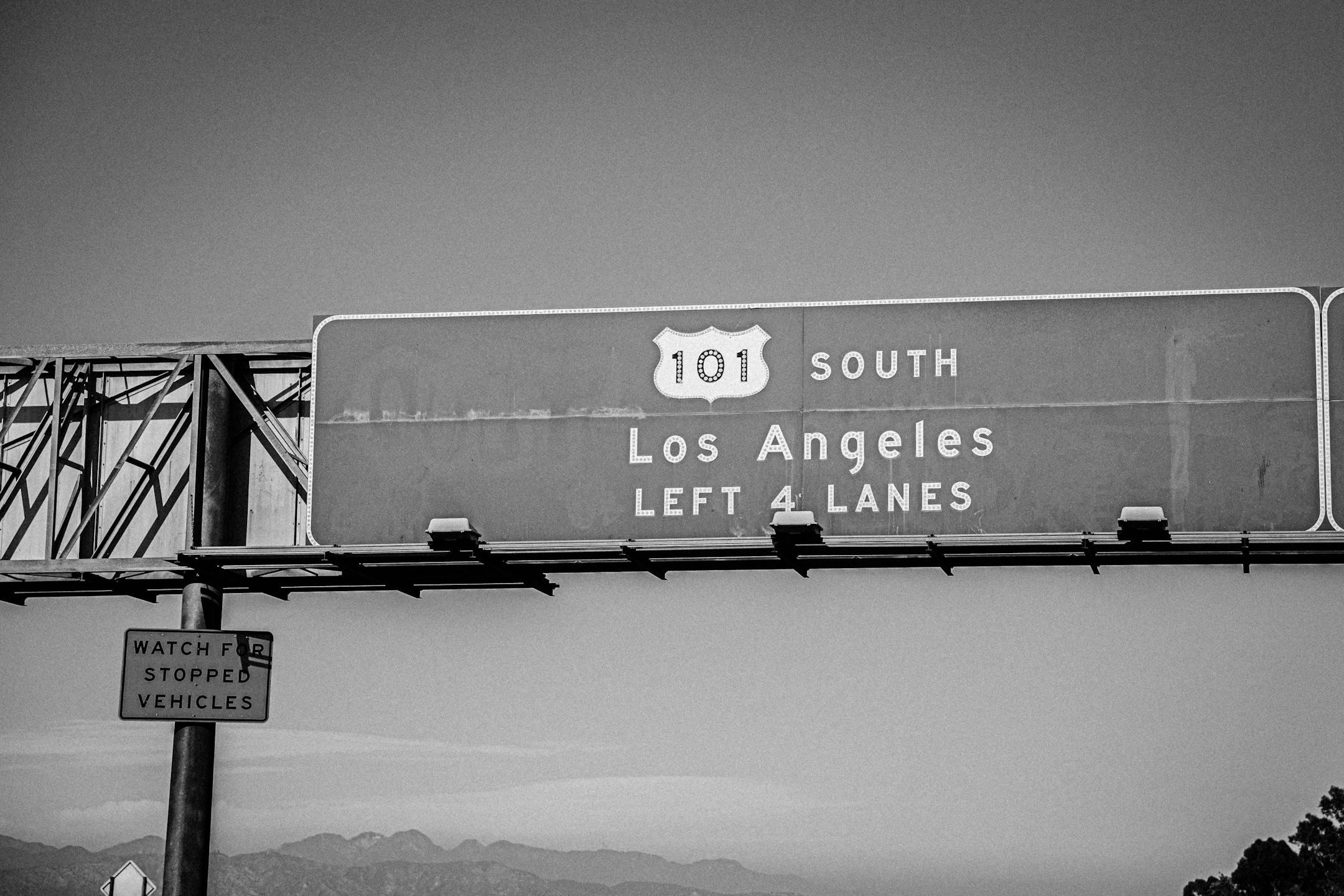 Monochrome image of Route 101 highway sign leading to Los Angeles, highlighting four lanes.