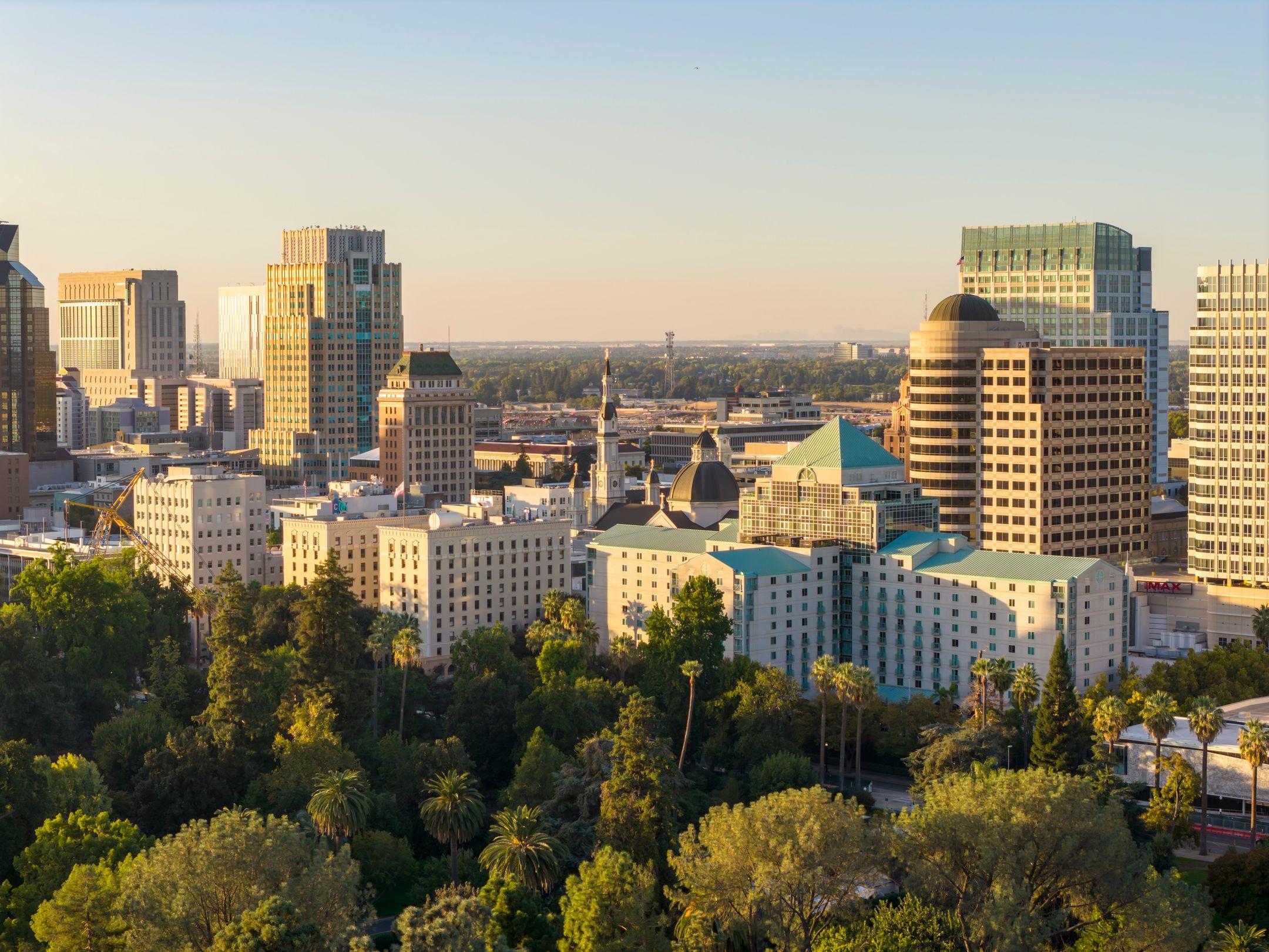 A stunning aerial view of downtown Sacramento skyline with lush greenery under the golden sunset light.