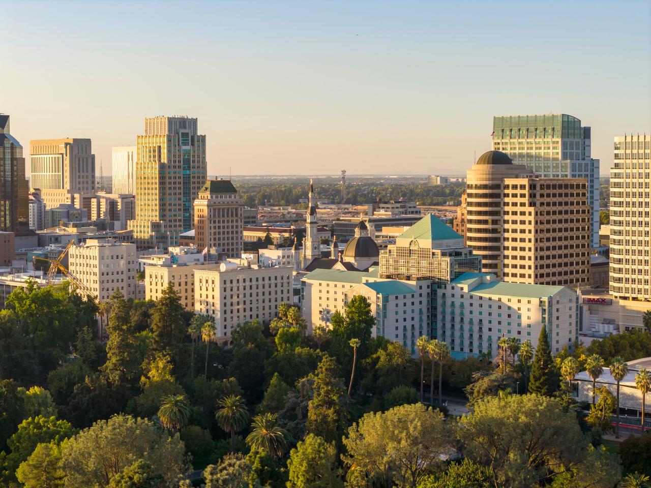 A stunning aerial view of downtown Sacramento skyline with lush greenery under the golden sunset light.