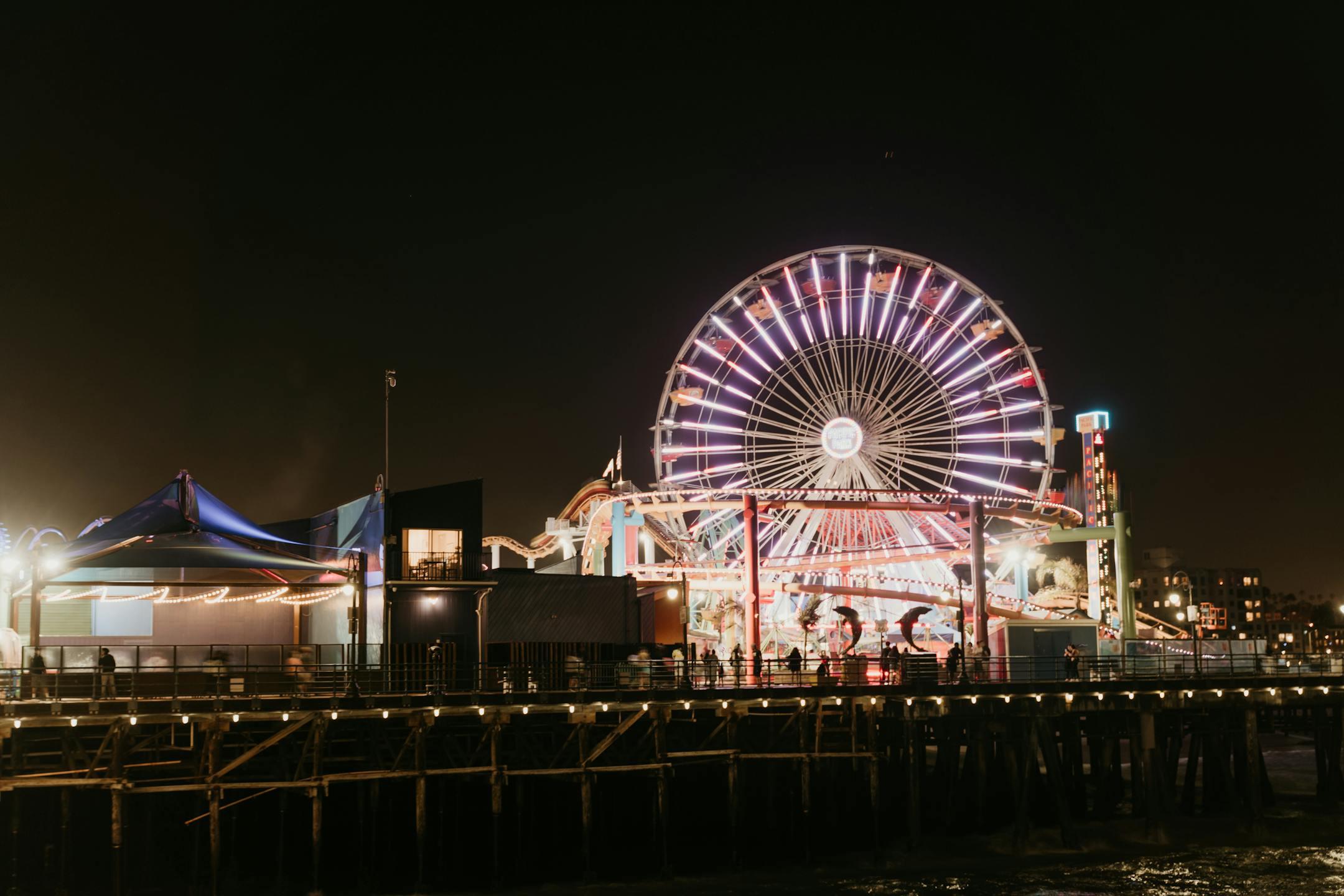 A vibrant Ferris wheel illuminates the Santa Monica Pier, creating a lively and colorful nighttime atmosphere.
