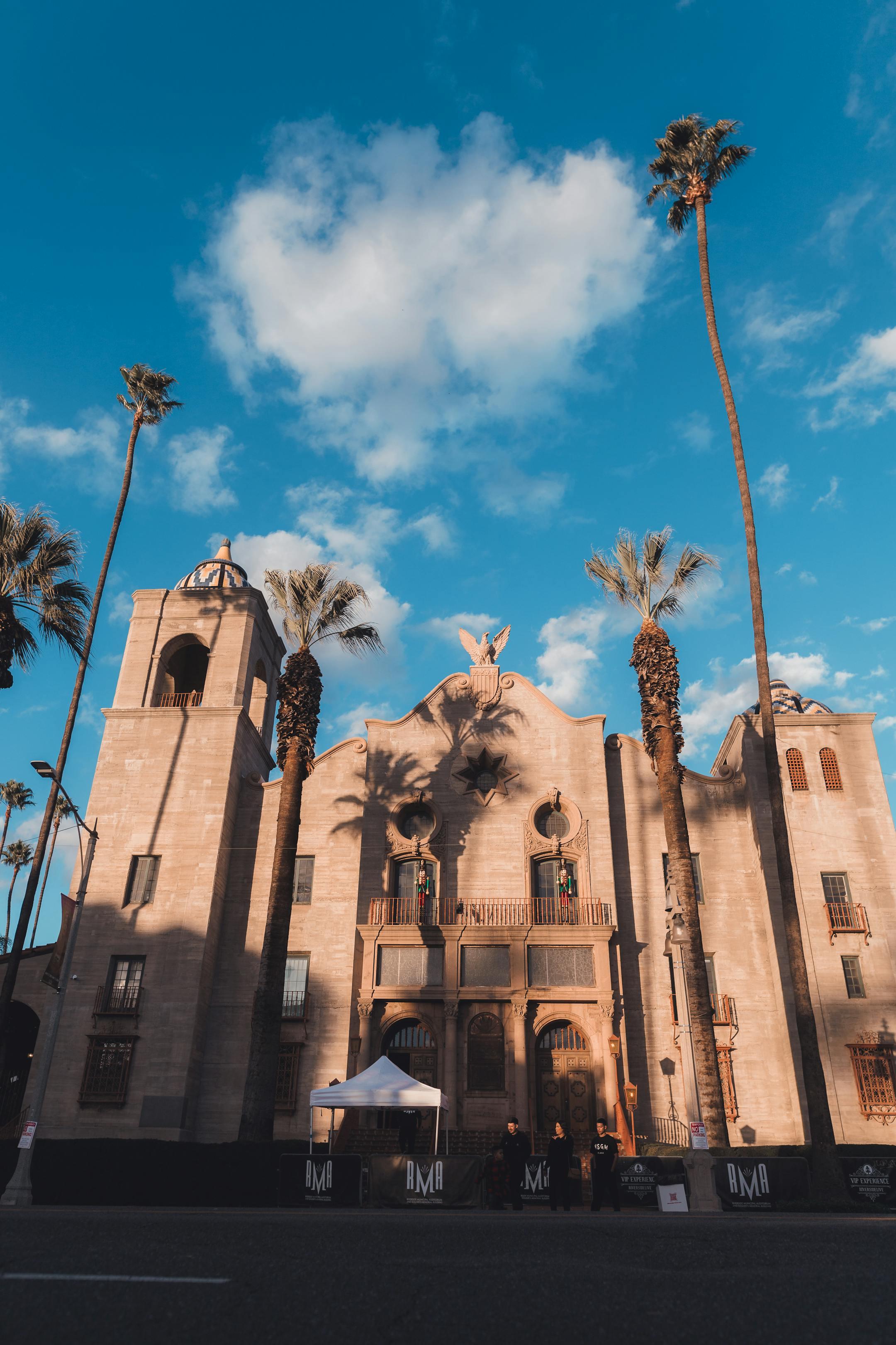 Low angle view of the Riverside Municipal Auditorium against a blue sky with palm trees.