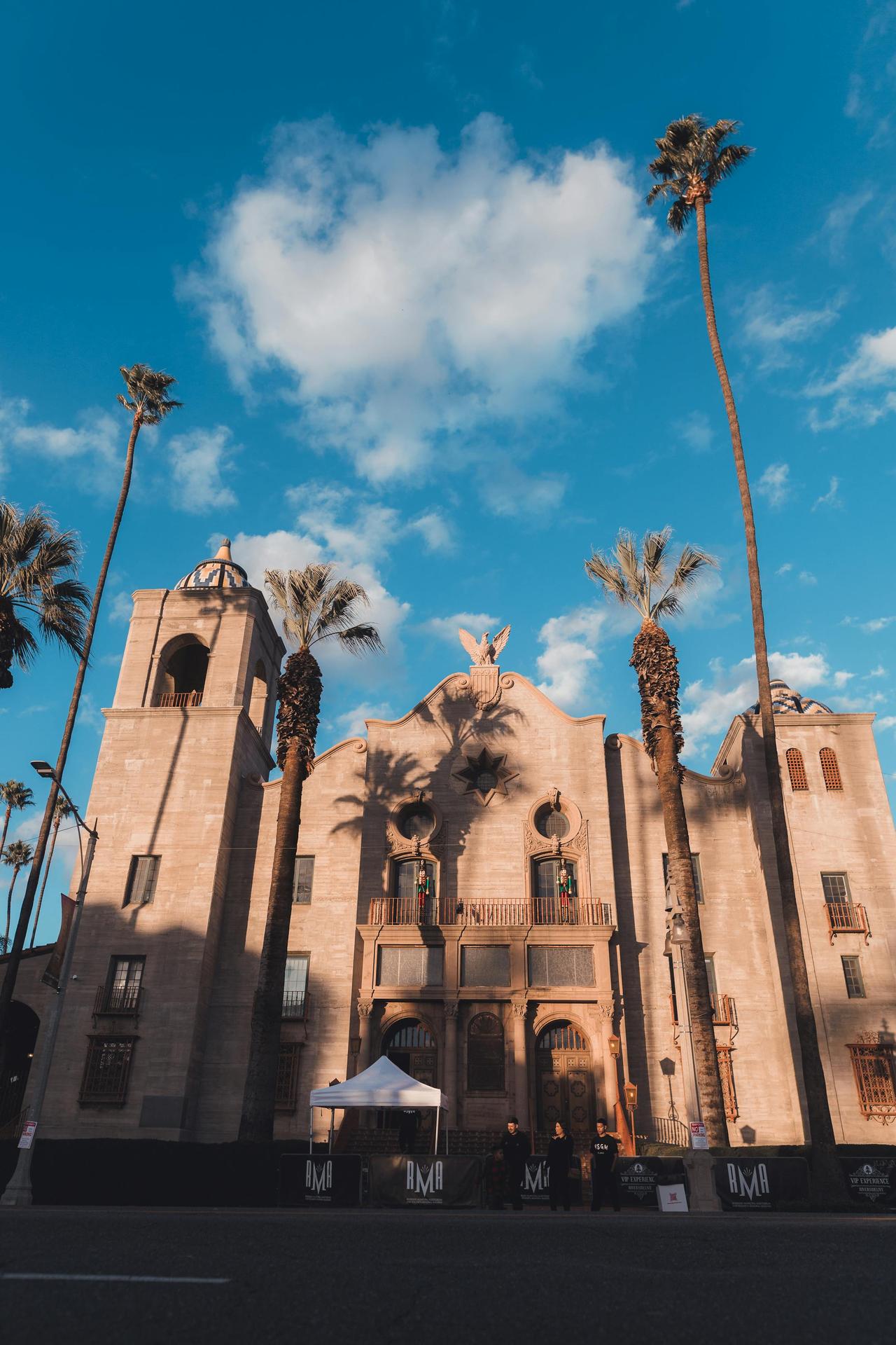 Low angle view of the Riverside Municipal Auditorium against a blue sky with palm trees.