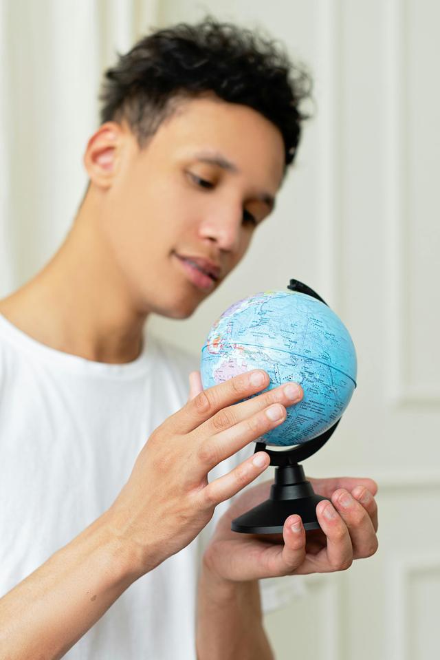 Young man examining a small blue globe indoors with keen interest.