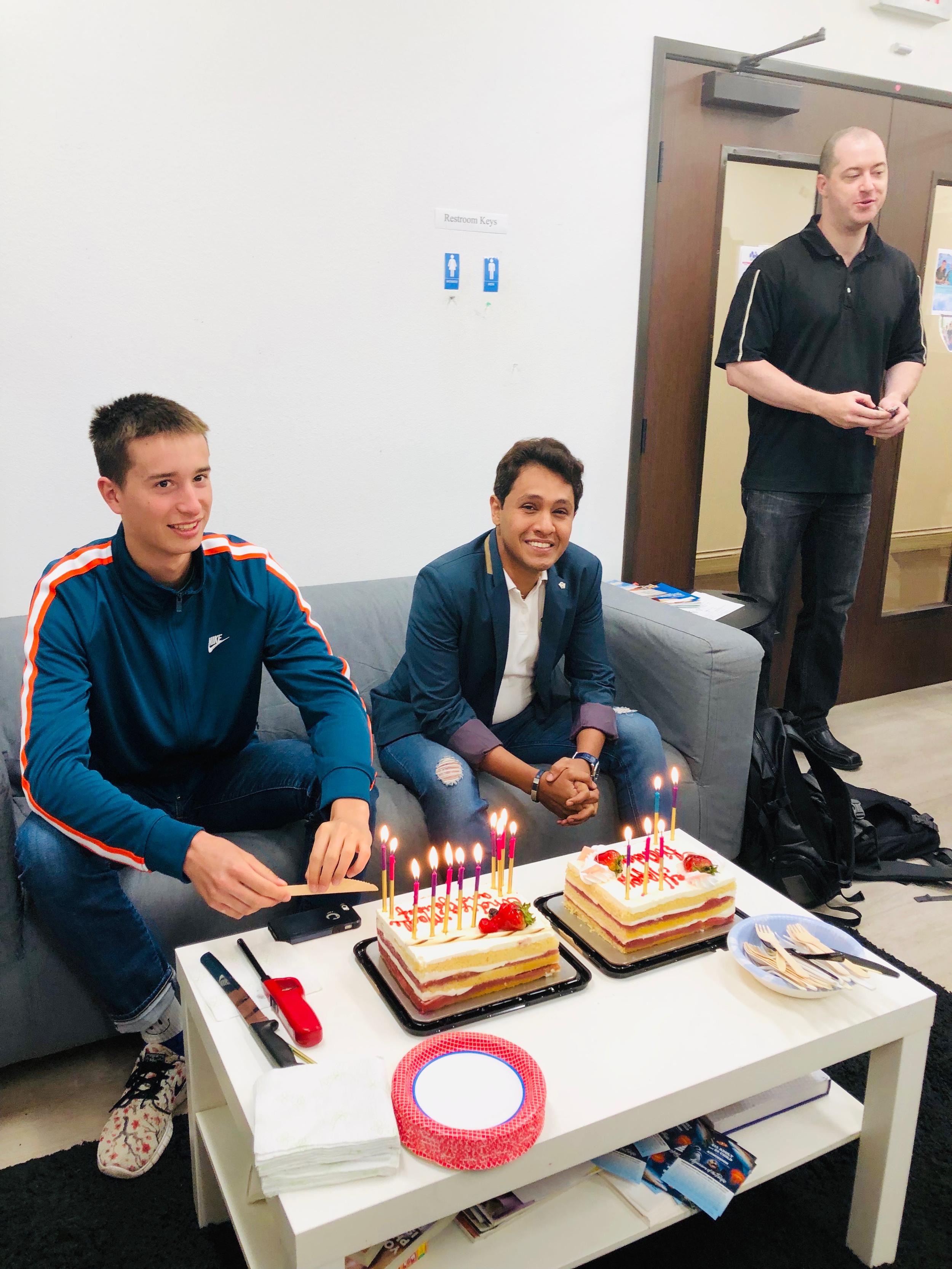 Two happy students on a couch, celebrating their brithday with two cakes in front of them on the table. The best way to understand how to learn English in the USA is through practicing with Americans.