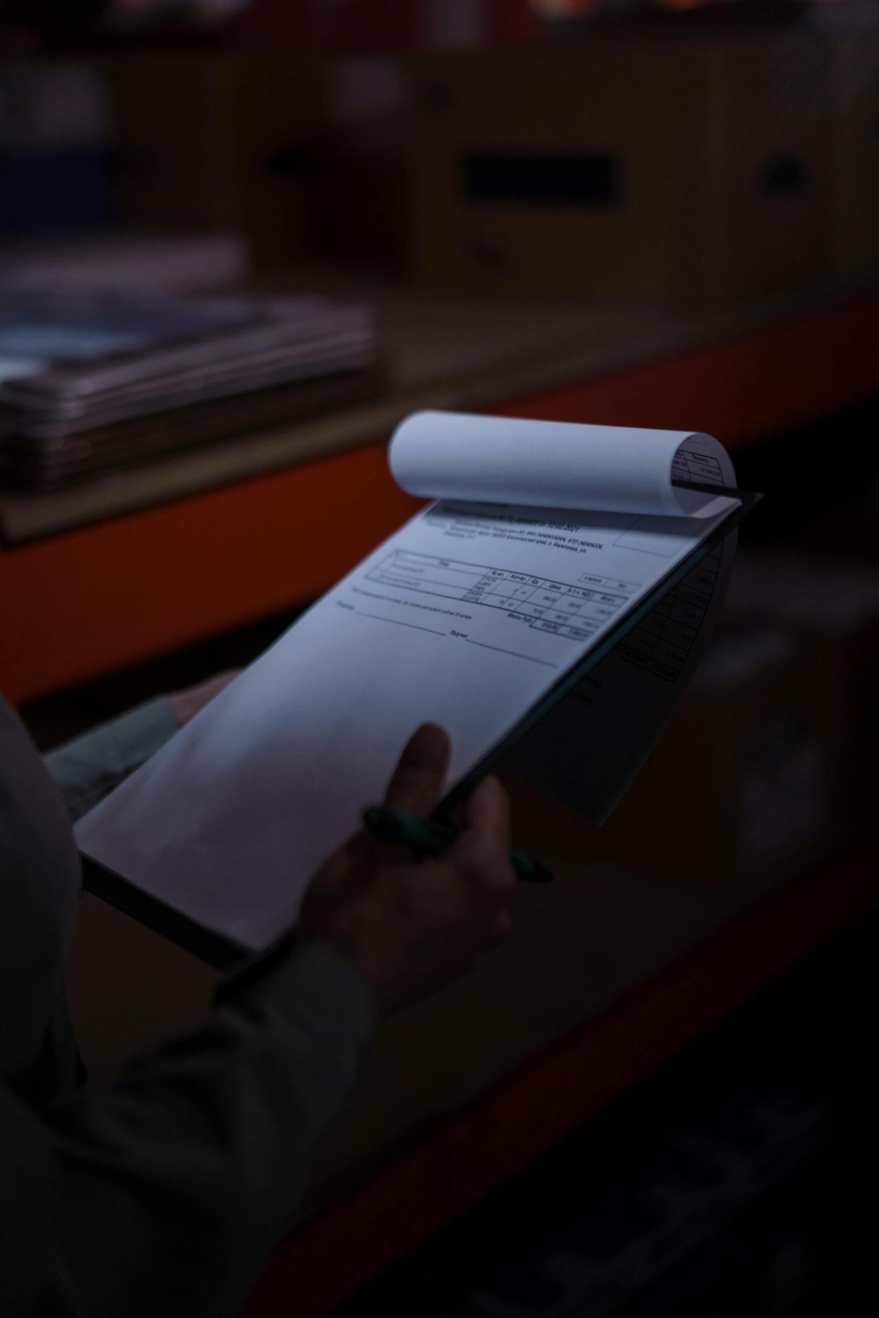 Silhouette of a person holding a clipboard with documents in a dimly lit warehouse.