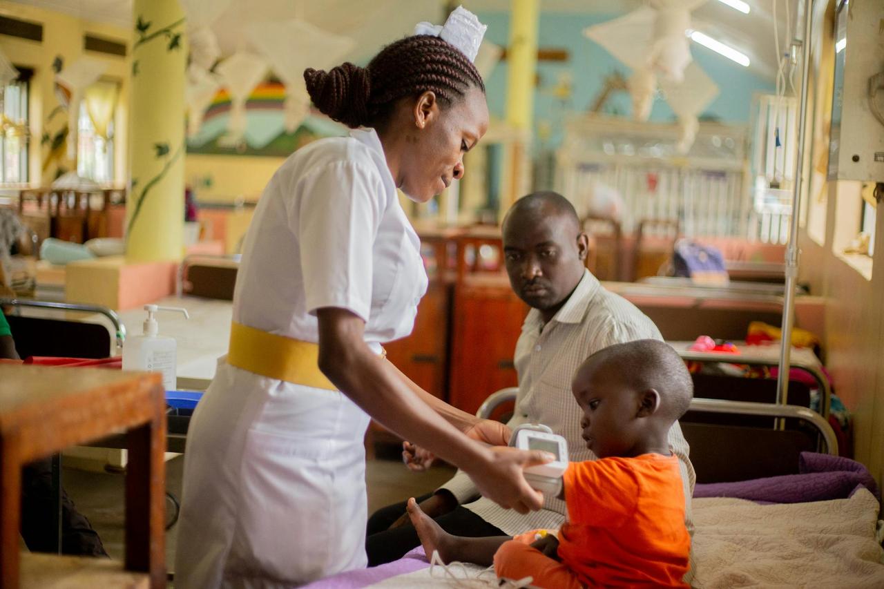 A nurse attends to a young patient while a guardian looks on in a hospital ward.