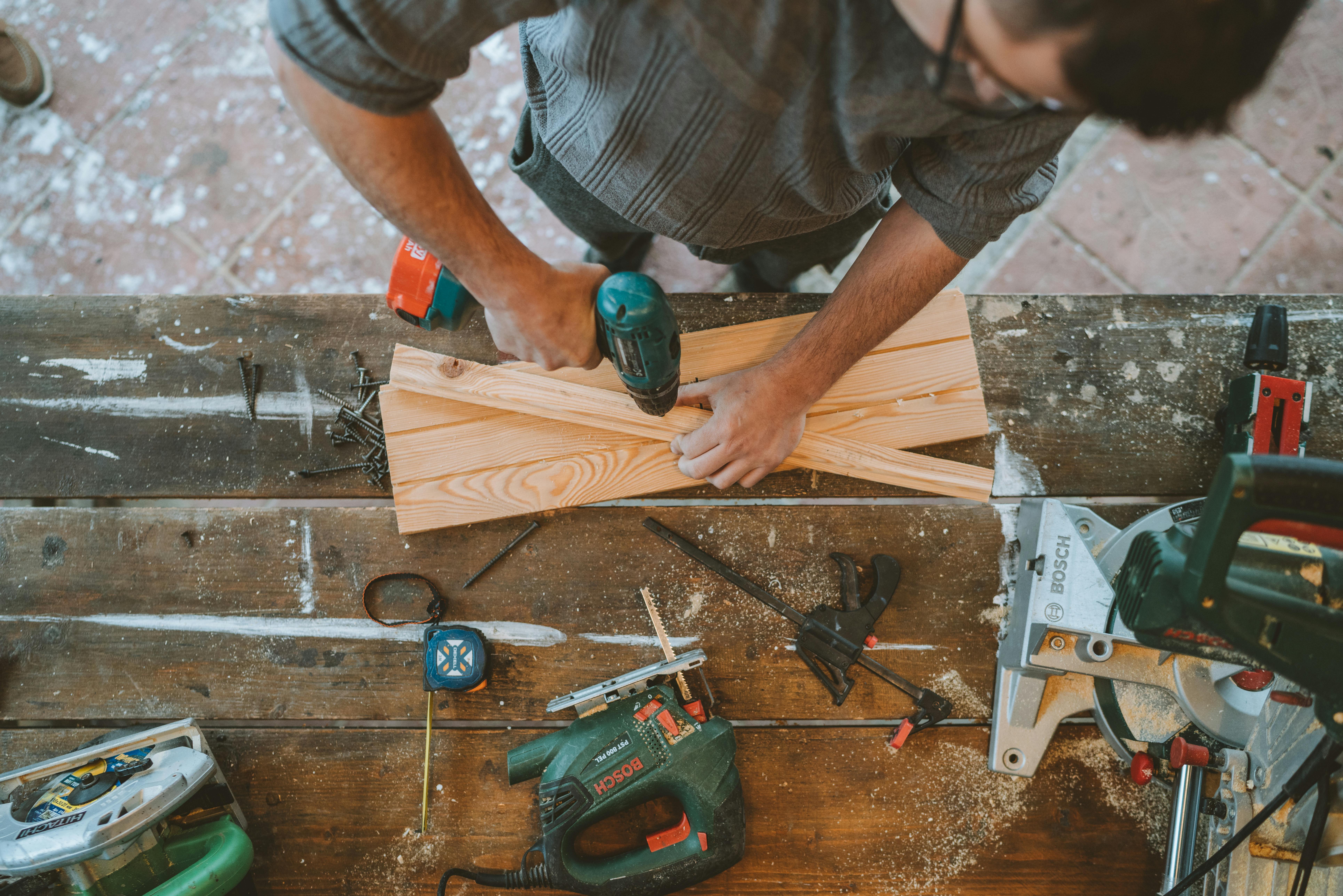 Handyman working with tools and drill on wooden surface