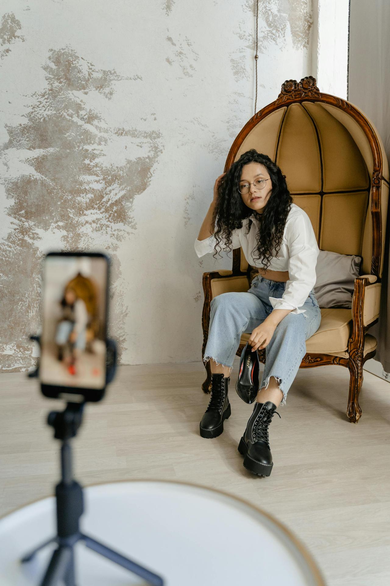 Young woman in trendy outfit sitting on a chair, recording indoors.