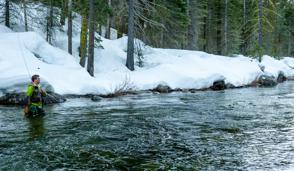 Fly fisherman making a cast while standing in a river with snow on the river bank