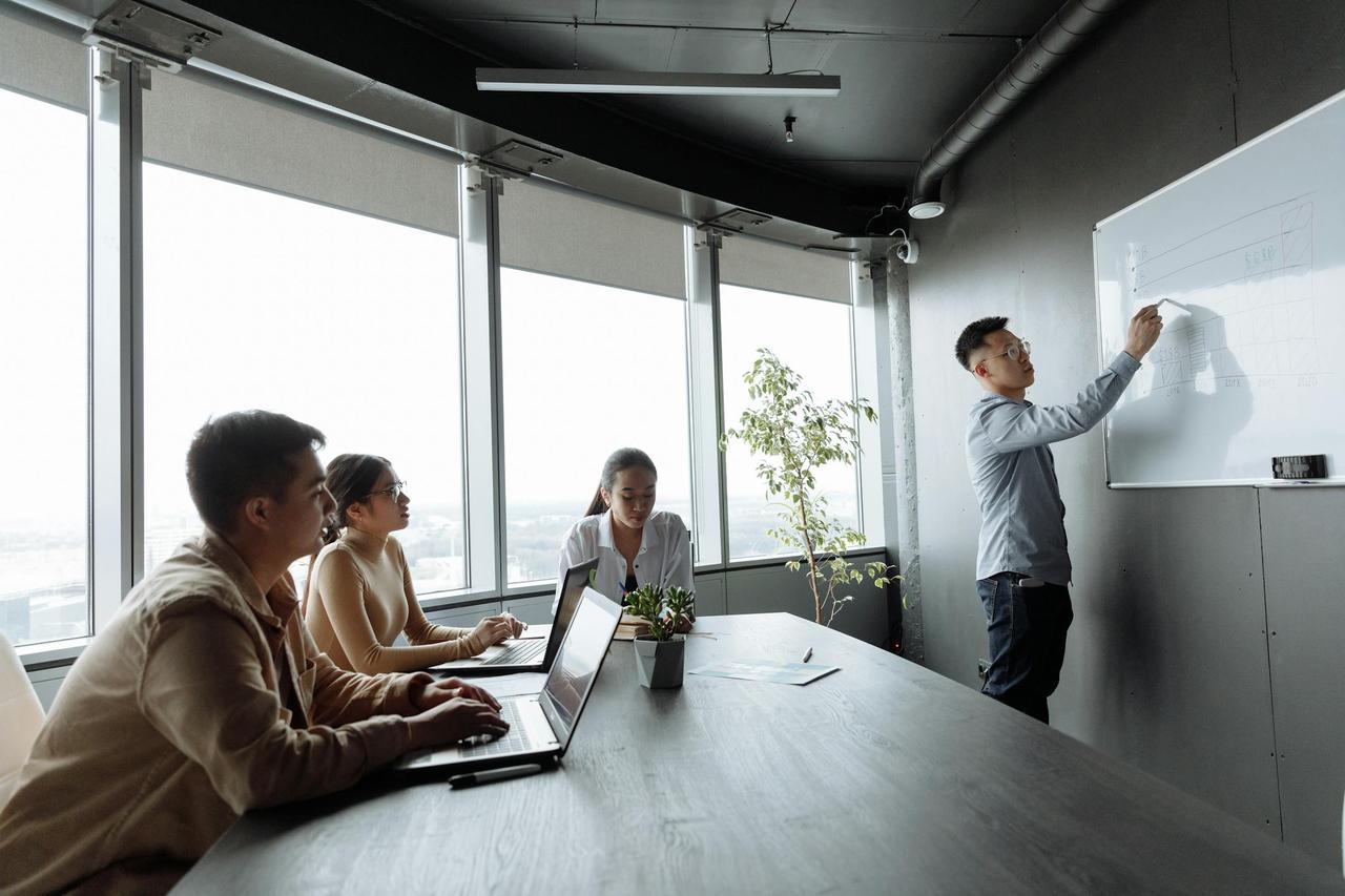 Diverse coworkers engaged in a whiteboard presentation in a well-lit office.