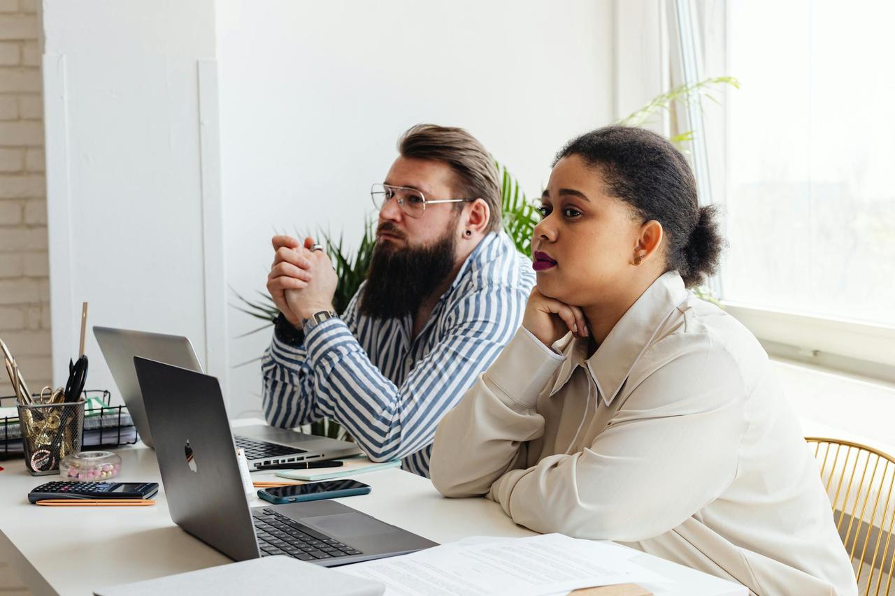 Two focused employees, a bearded man and a woman, attentively listening during a workspace meeting.