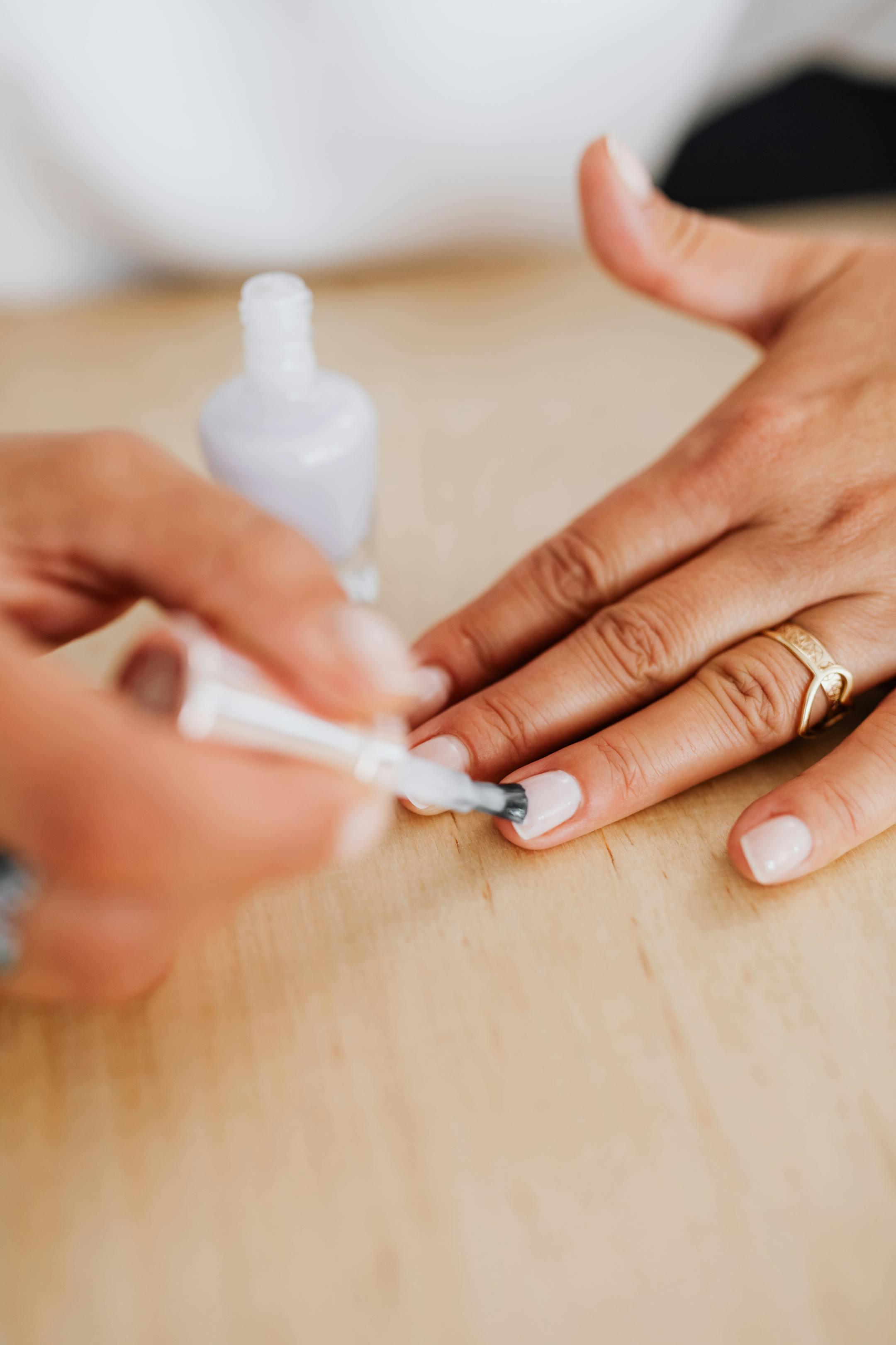 A detailed view of hands applying nail polish on natural nails with a gold ring.