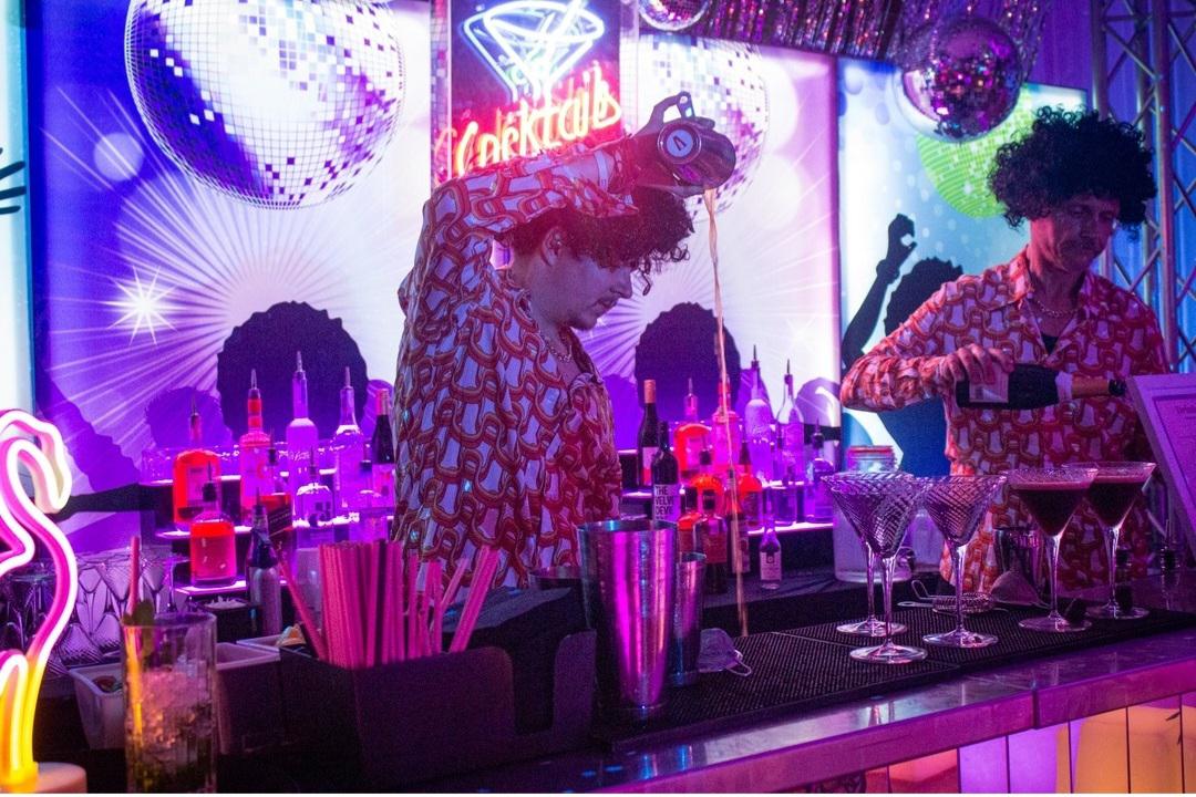 two-male-bartenders-wearing-fun-curly-wigs-serving-cocktails-behind-a-bar..jpg