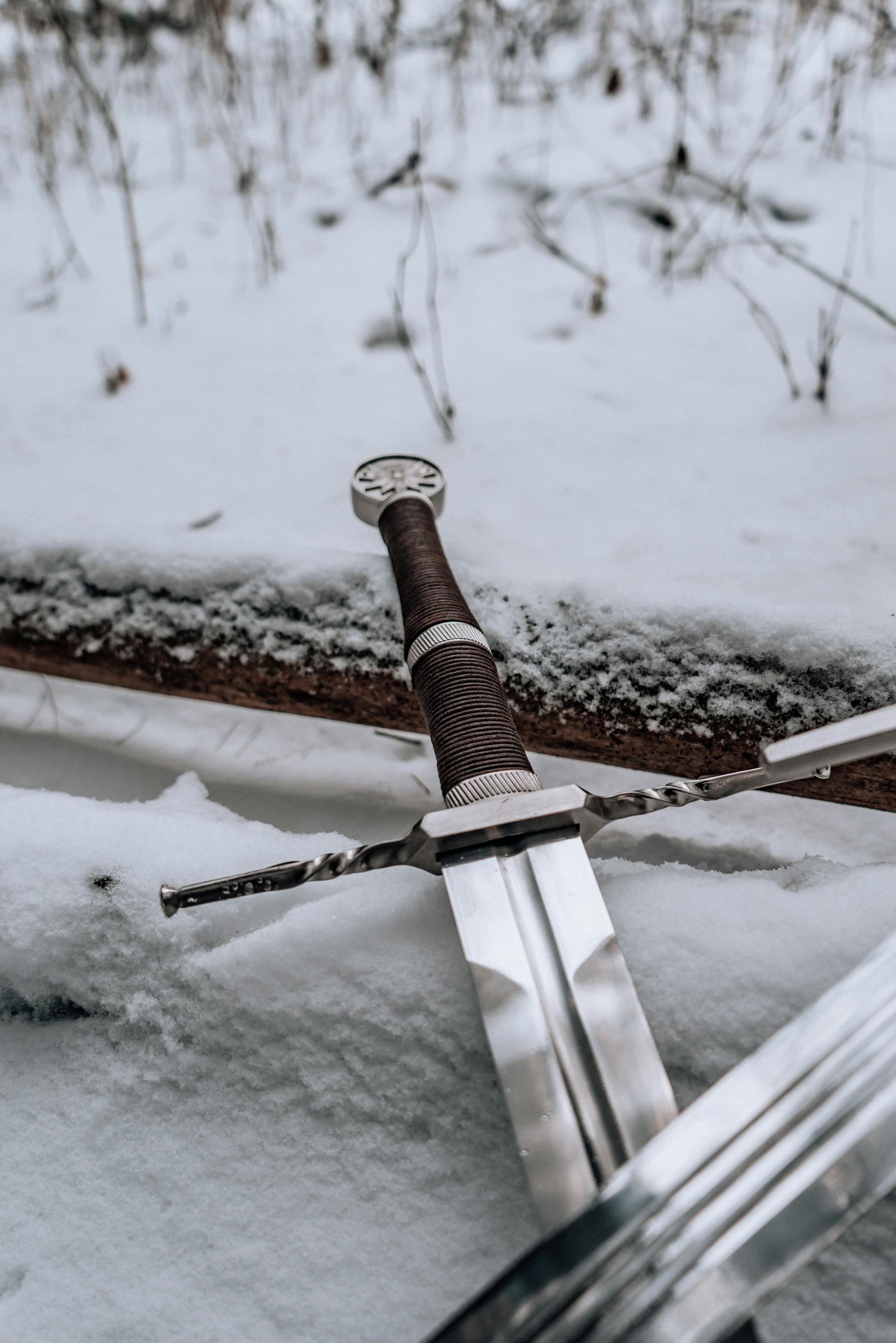 A close-up of a medieval sword lying in the snow, conveying a wintery historic theme.