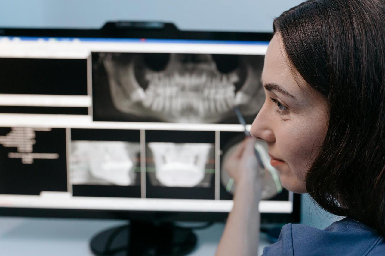 Female dentist reviewing digital dental x-rays on a computer screen in a clinic setting.