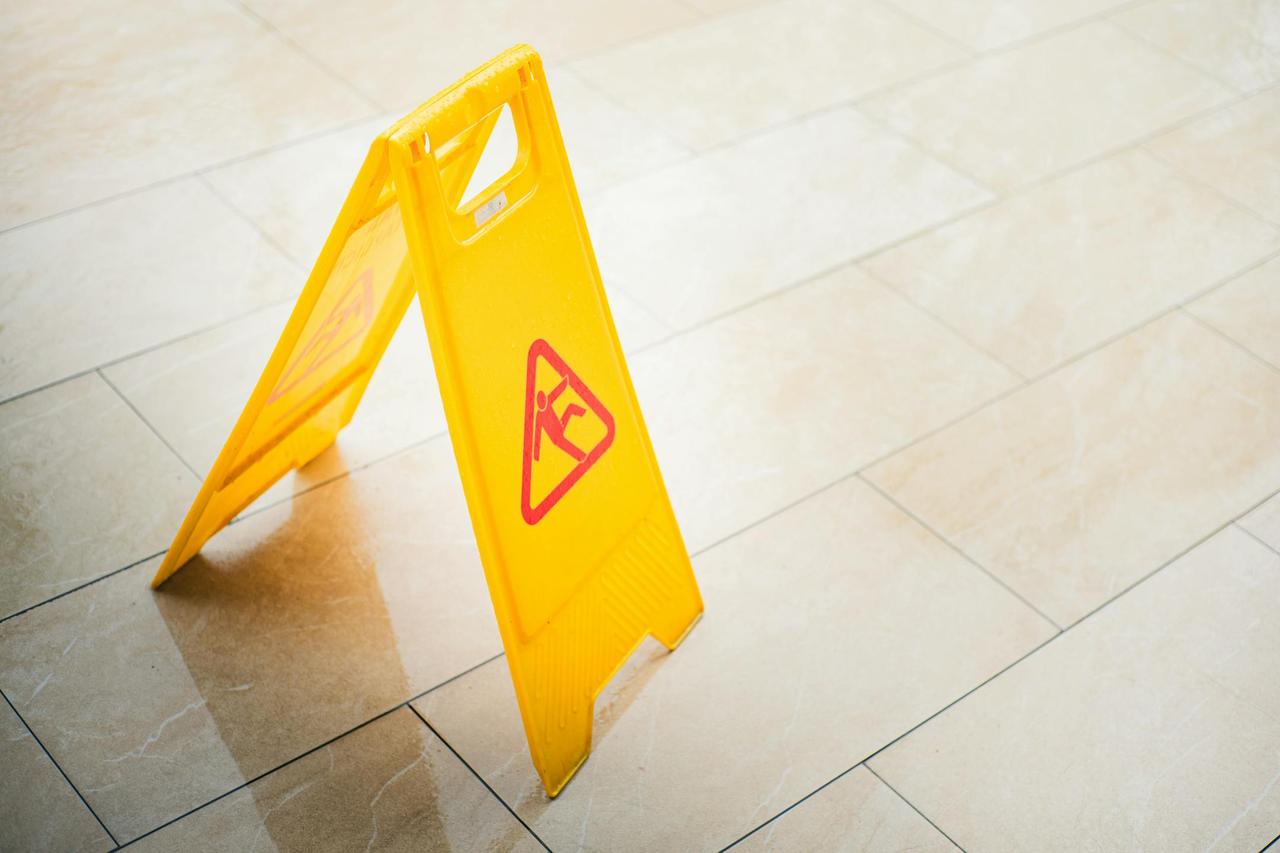A bright yellow caution sign on a tiled floor indicates a wet surface, alerting passersby to potential hazards.