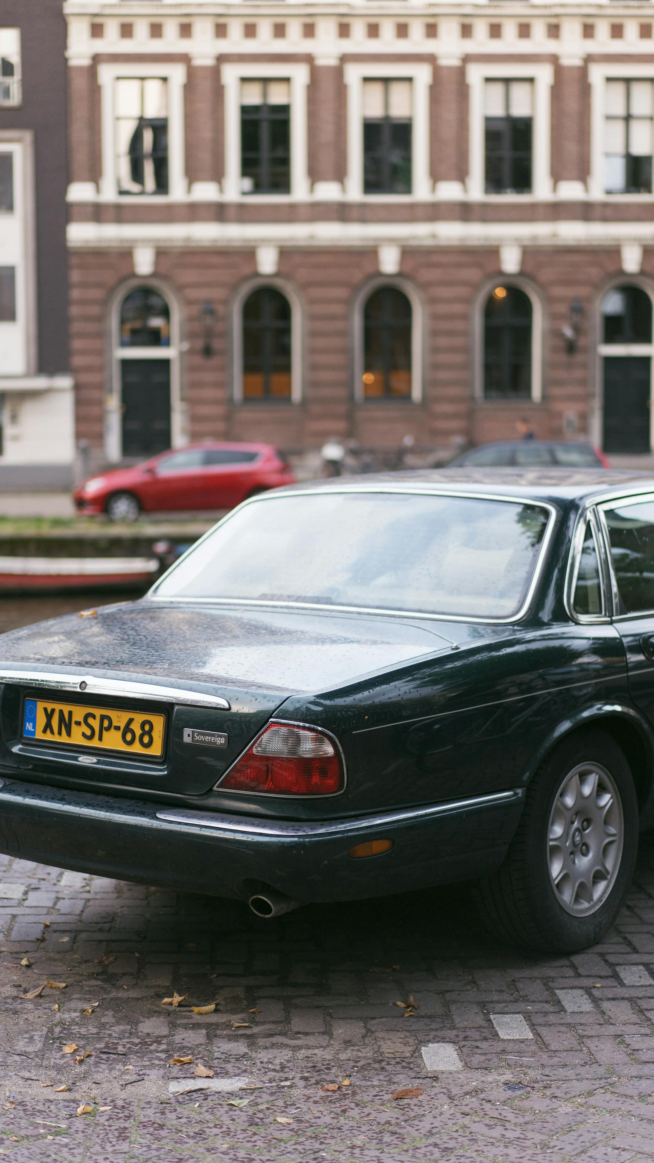 Vintage black Jaguar parked on cobblestoned street with European architecture backdrop.