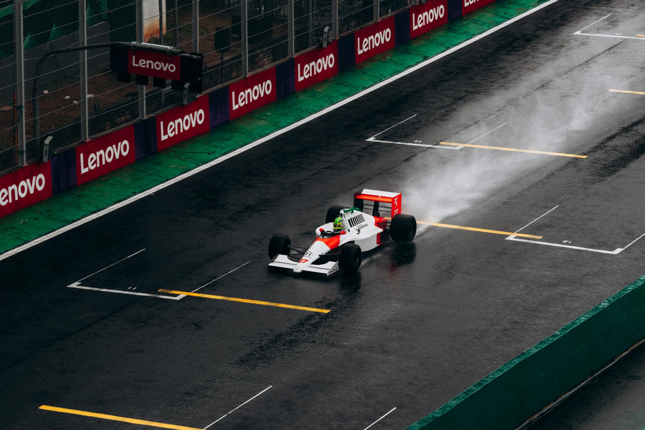 A classic Formula 1 car races on a wet track at Interlagos, Brazil, leaving a trail of spray behind.