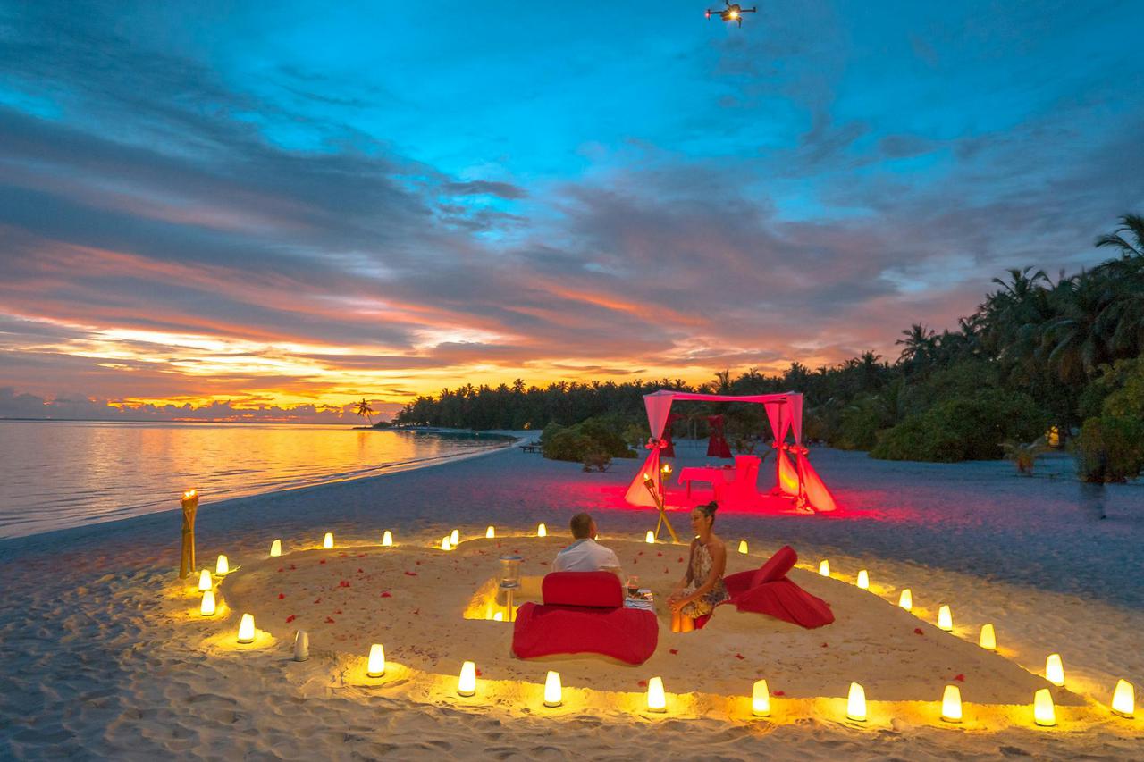 A romantic dinner setup on a beach with lanterns at sunset, perfect for a couple’s getaway.