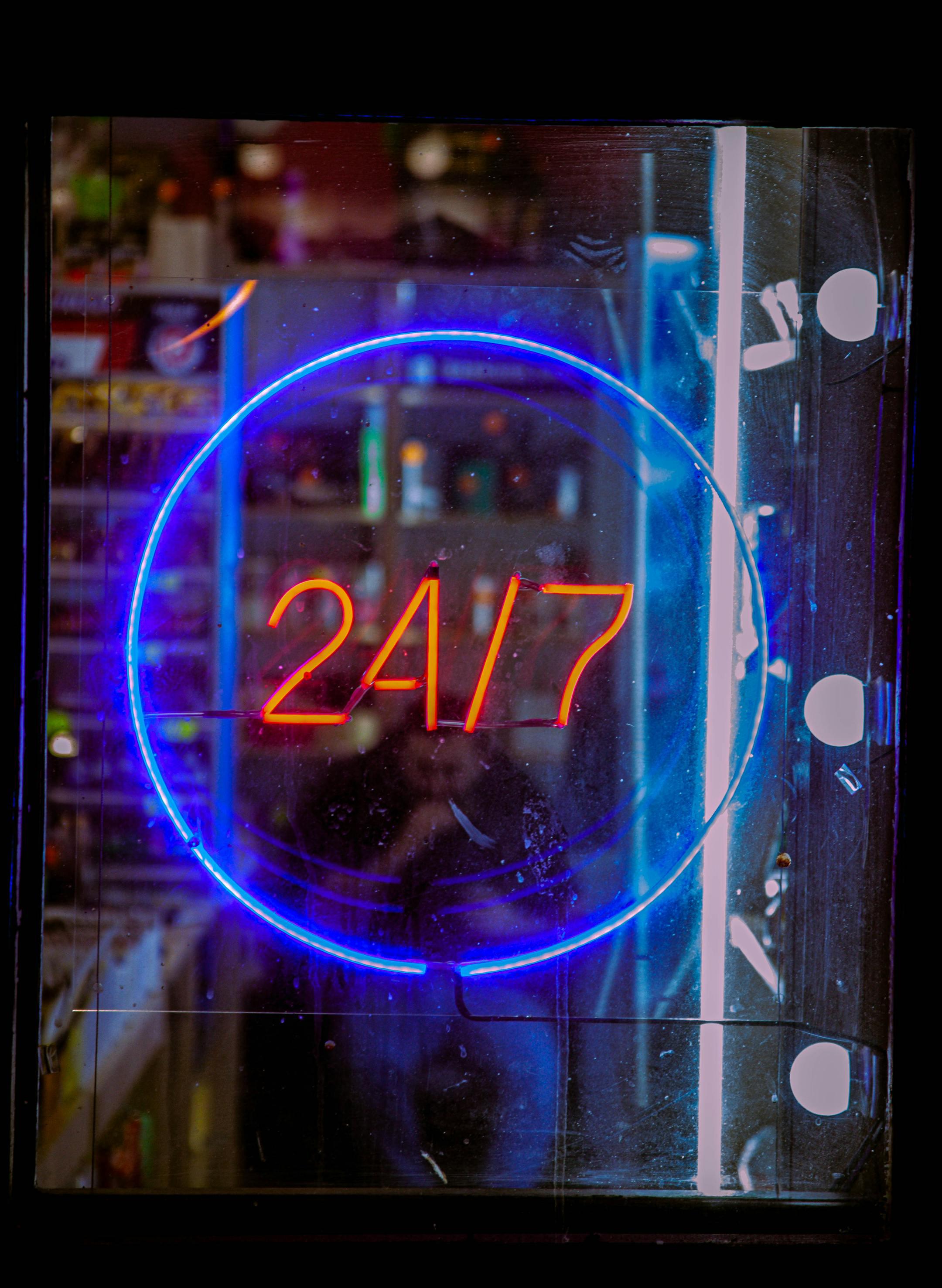 Vibrant neon blue and red 24/7 sign glowing in a shop window at night, creating a bustling urban vibe.