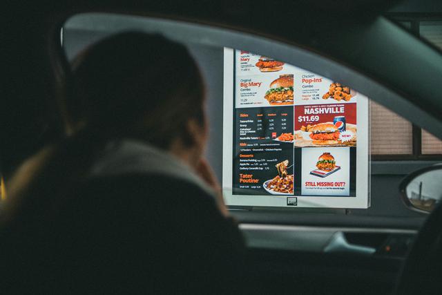 A woman in a car views the menu at a fast food drive-thru, ready to order her meal.