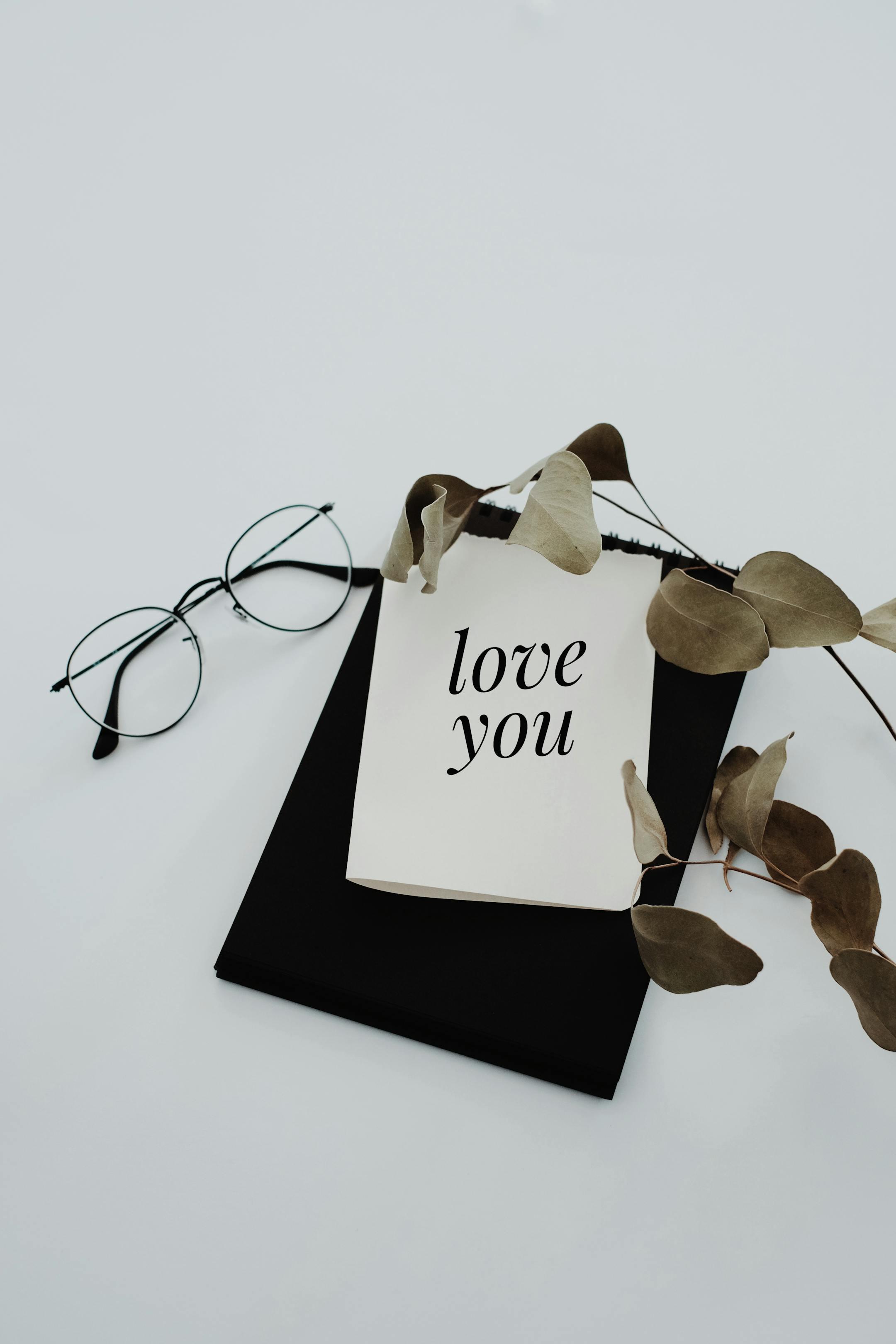 Elegant flat lay featuring a love note, eucalyptus leaves, and eyeglasses on a white background.