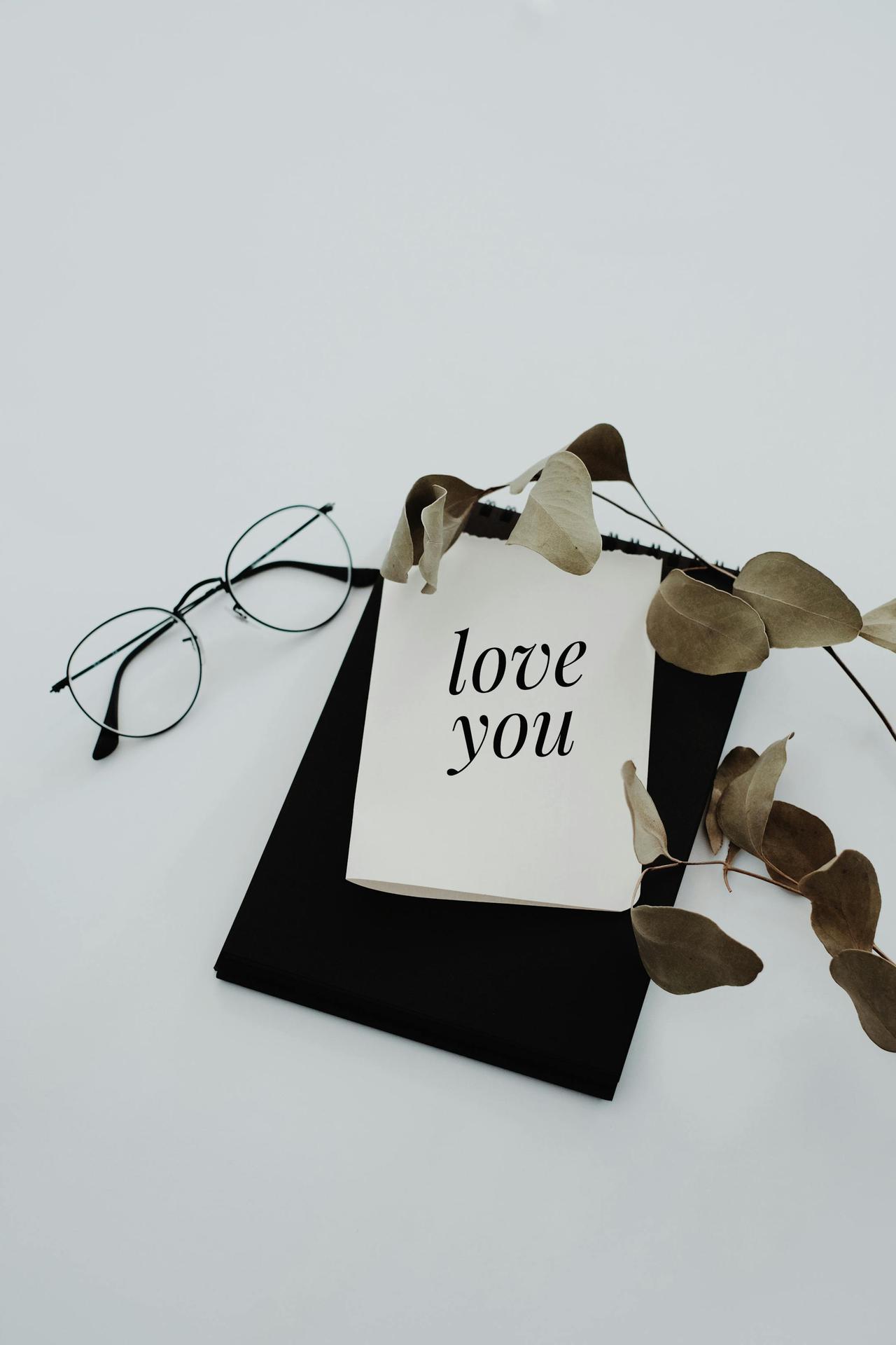 Elegant flat lay featuring a love note, eucalyptus leaves, and eyeglasses on a white background.