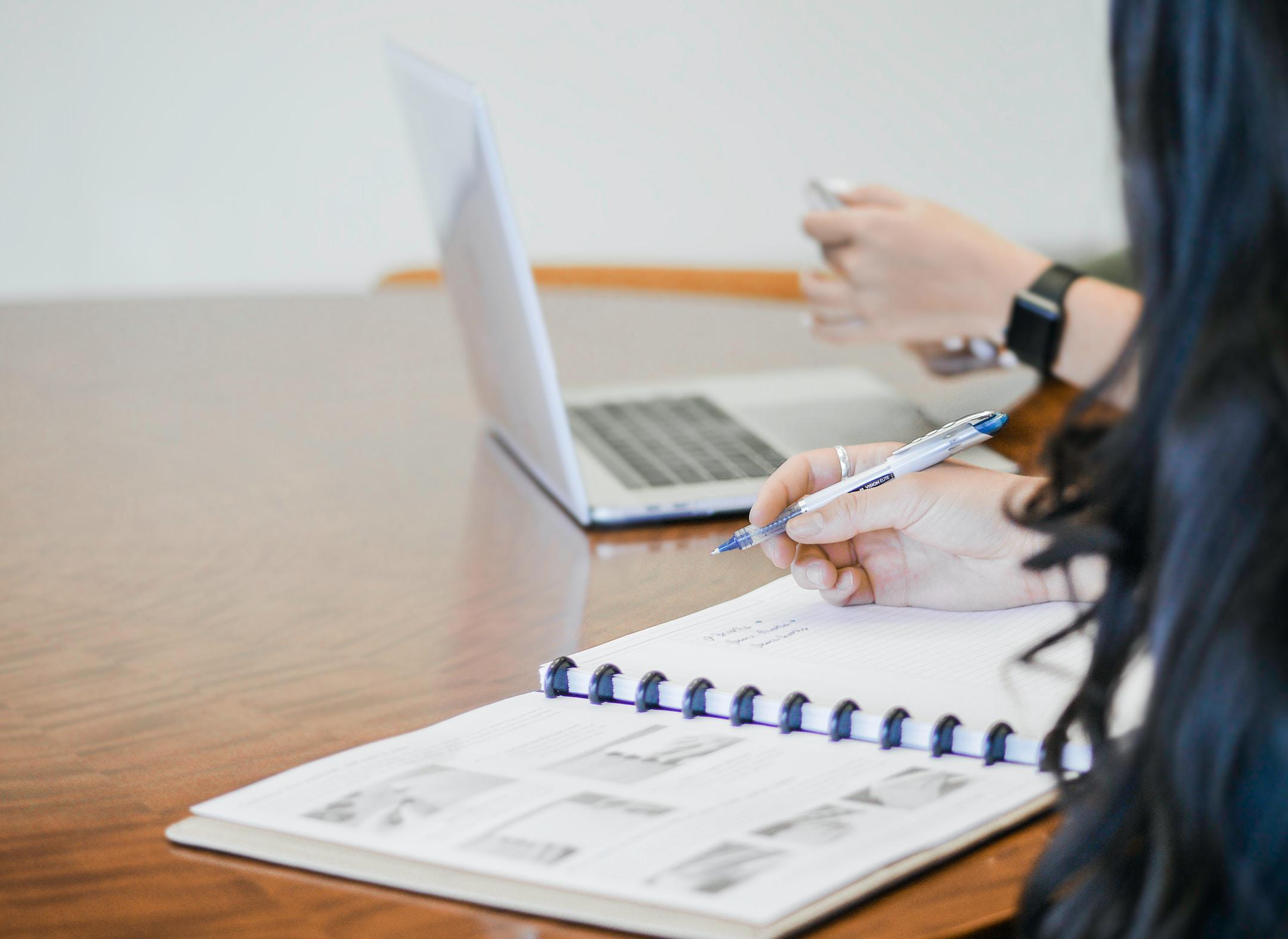 A person with a pen and a person on a laptop reviewing strategy and conducting project performance measurment in Burlington, MA.