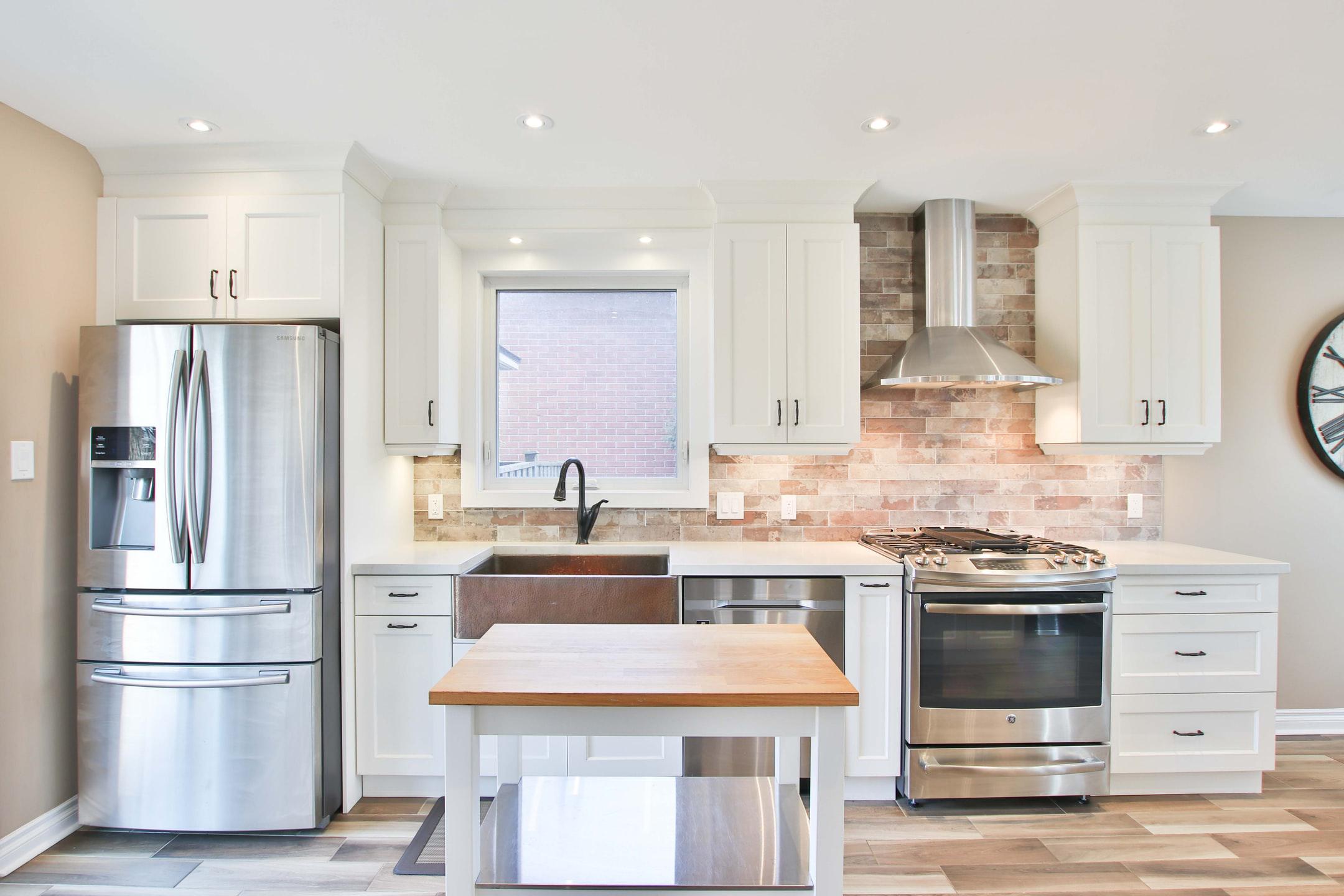 A modern kitchen with an island, wood floors, white cabinets, and a steel fridge.