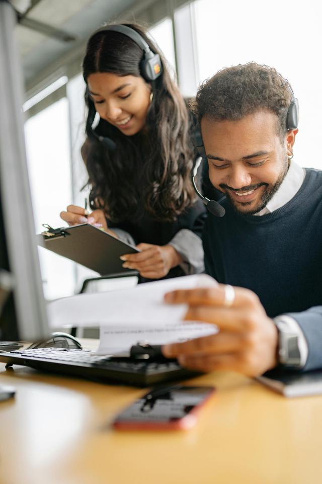 Two diverse call center employees collaborating with documents and headsets.