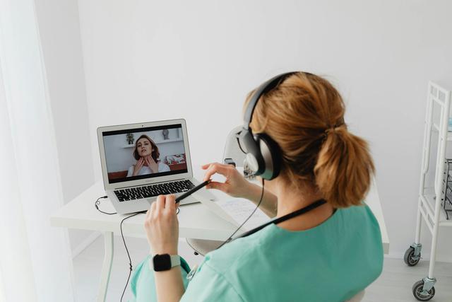 A doctor conducting an online consultation with a patient via laptop in a modern office setting.