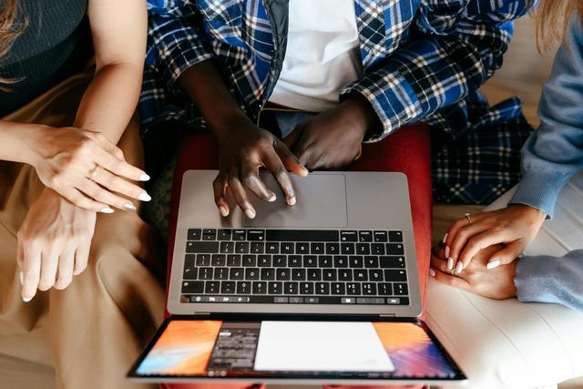 Three diverse people collaborating over a laptop, working closely on a project in a casual setting.