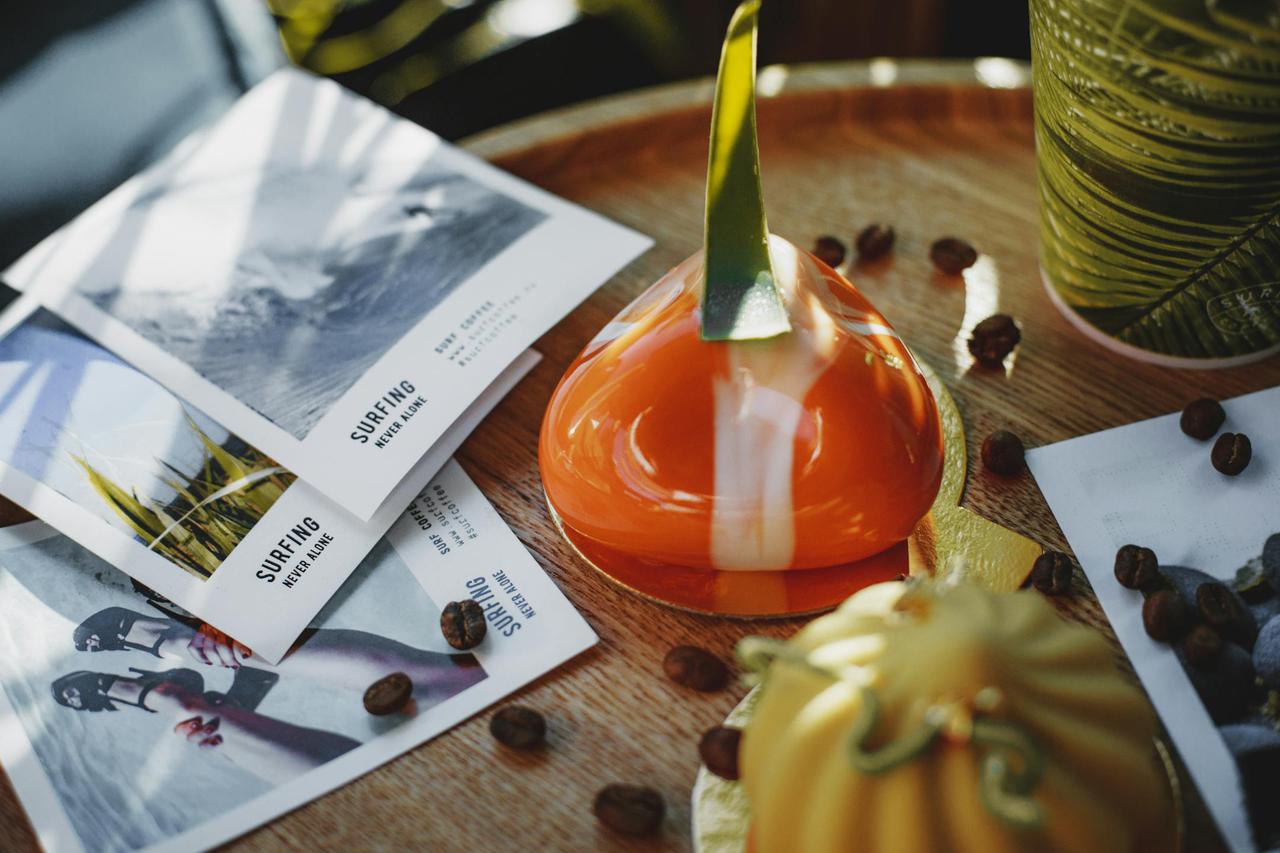 Artistic shot of gourmet pastries with coffee beans and surf-themed flyers on a wooden table.