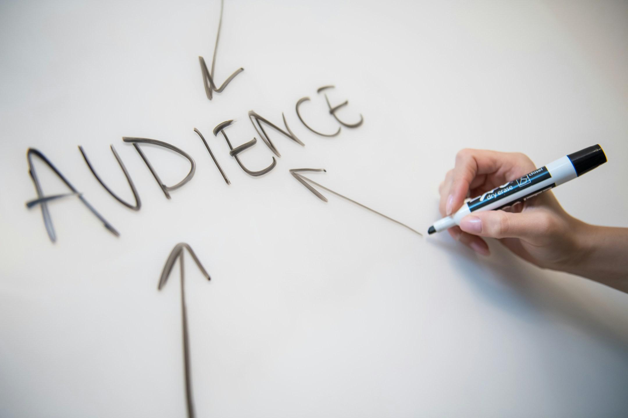 Woman's hand writing the word "audience" on a whiteboard, with