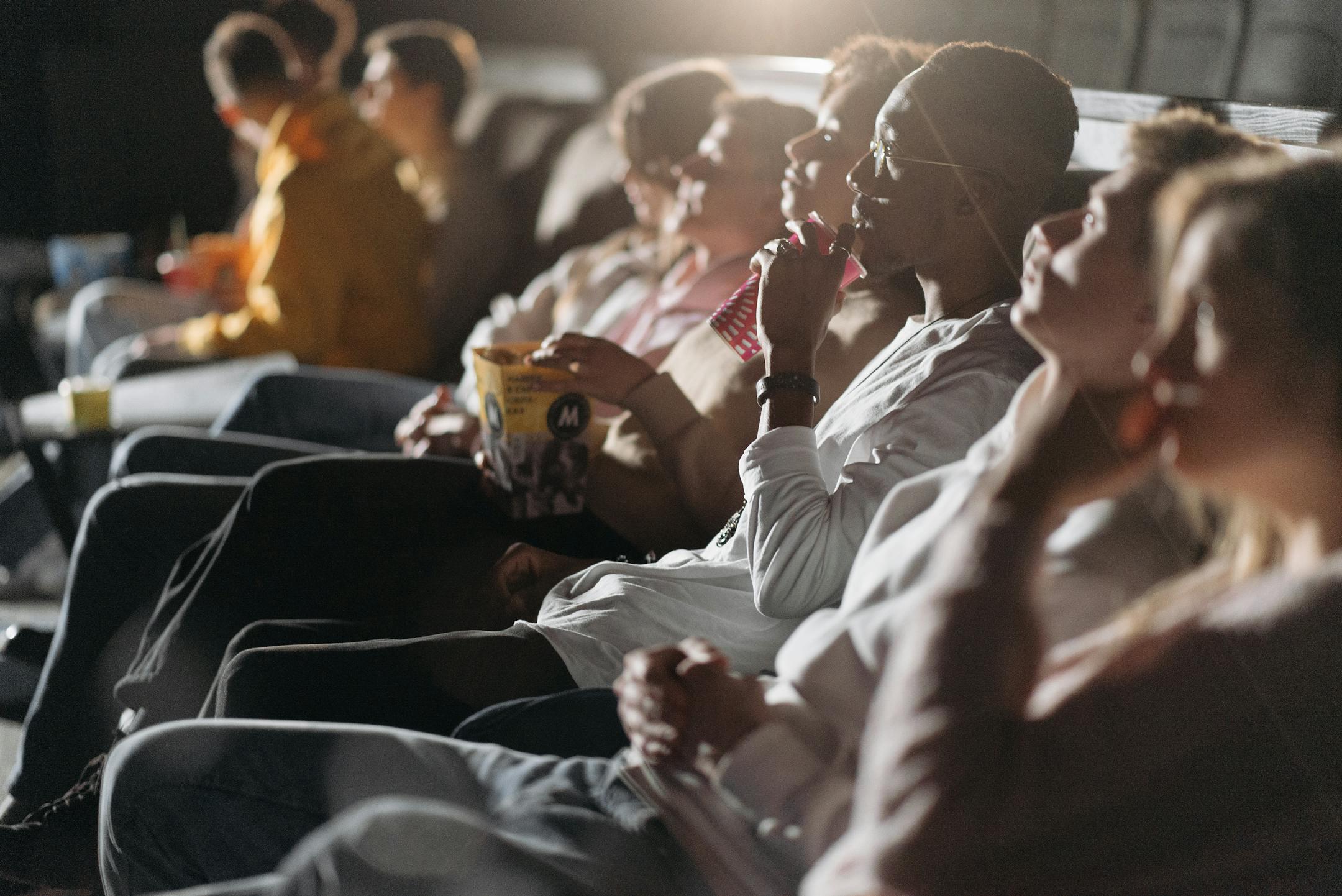 A group of people enjoying a movie in a theater, sipping drinks and eating popcorn.