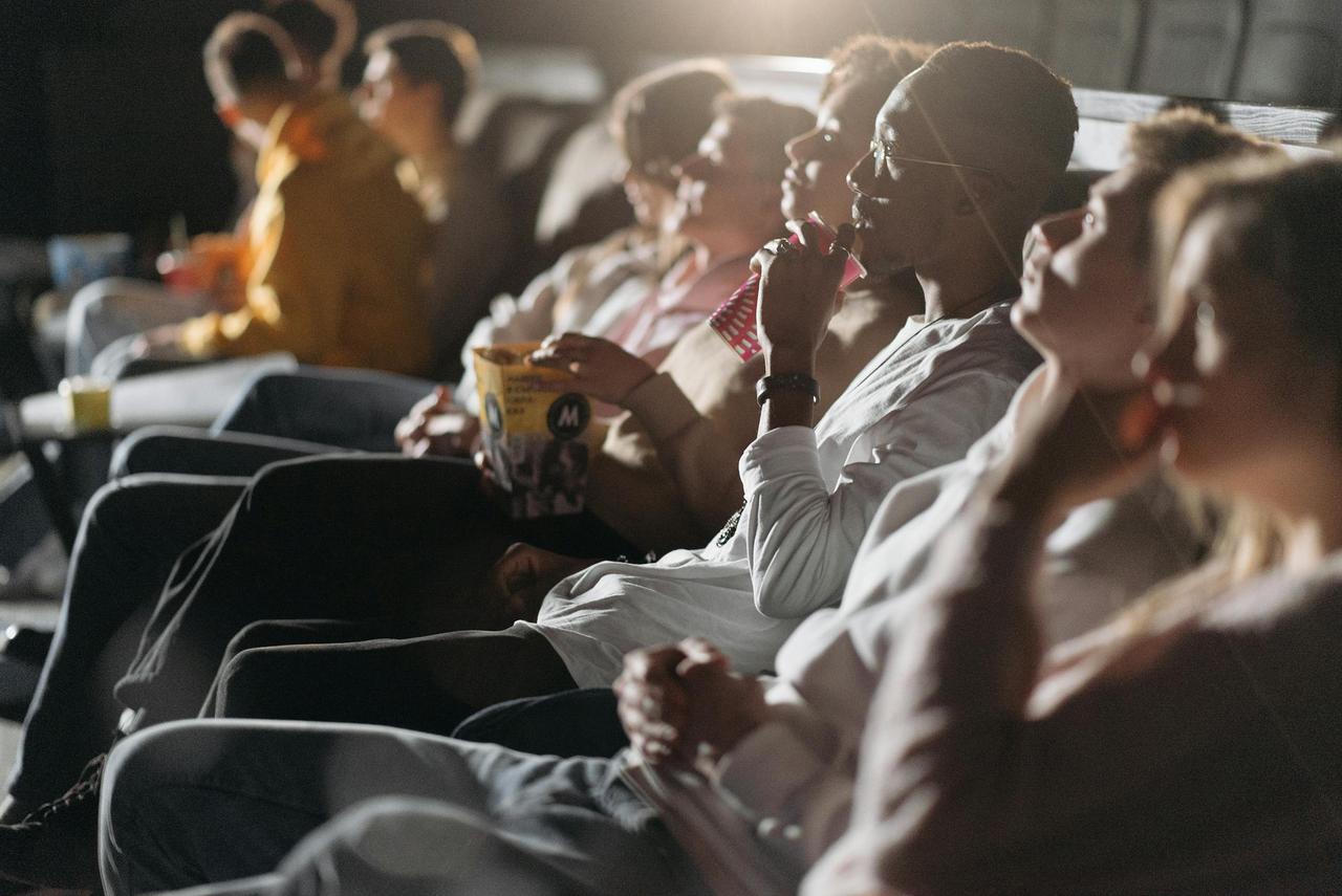 A group of people enjoying a movie in a theater, sipping drinks and eating popcorn.